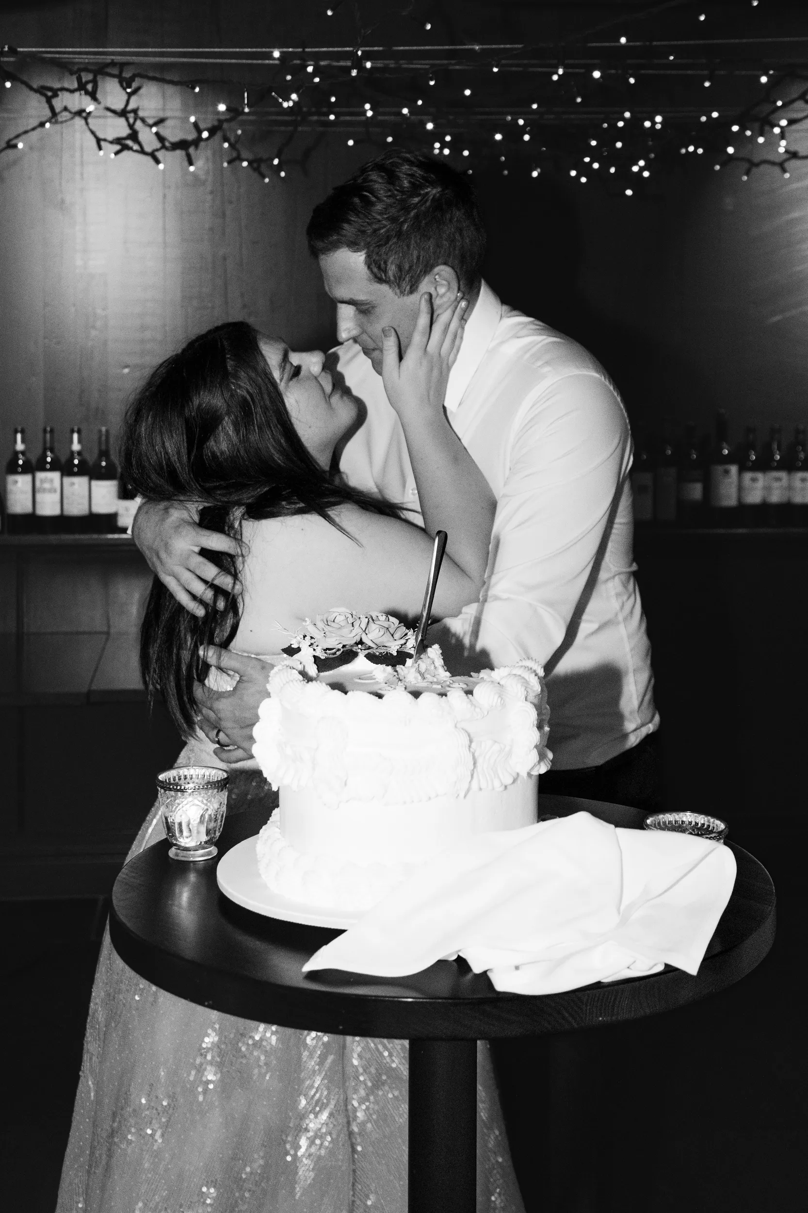 Carlie and Iain black and white cake cutting moment in rustic cellar with string lights and exposed brick