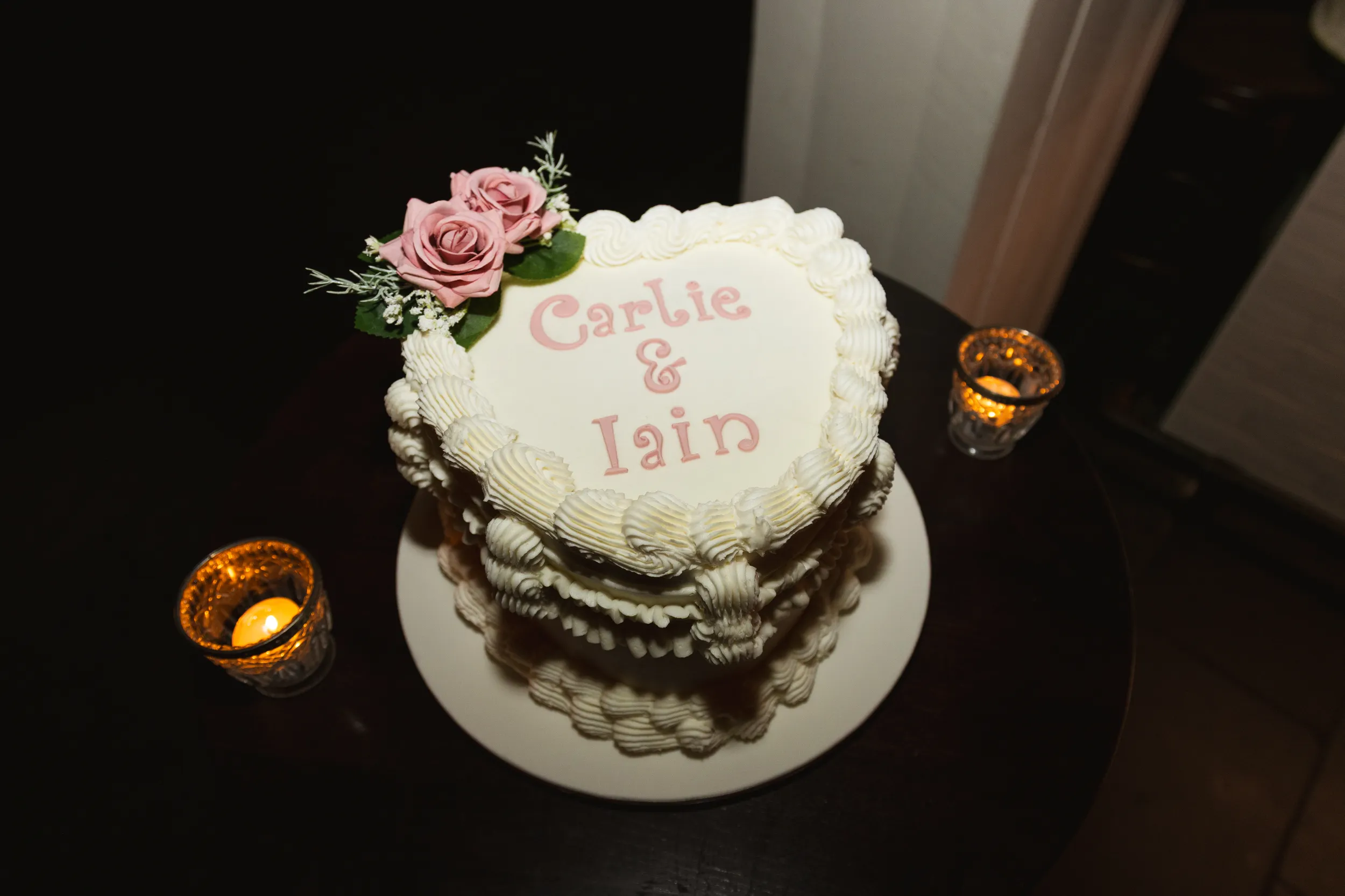Beautiful personalized wedding cake with Carlie & Iain written in pink icing, decorated with pink roses and candles