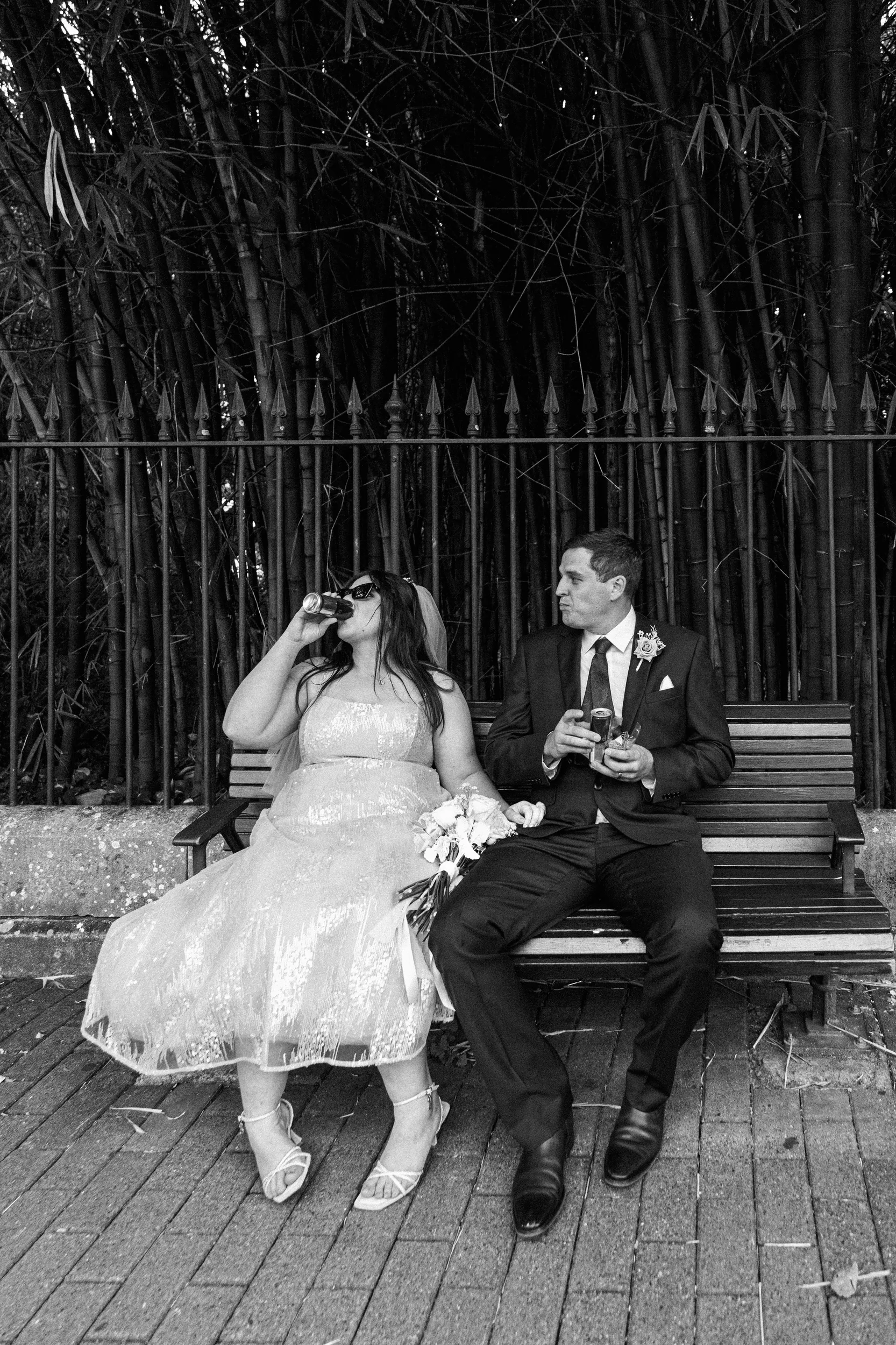 Carlie and Iain casual black and white moment sitting on wooden bench with drinks, both appearing relaxed and happy