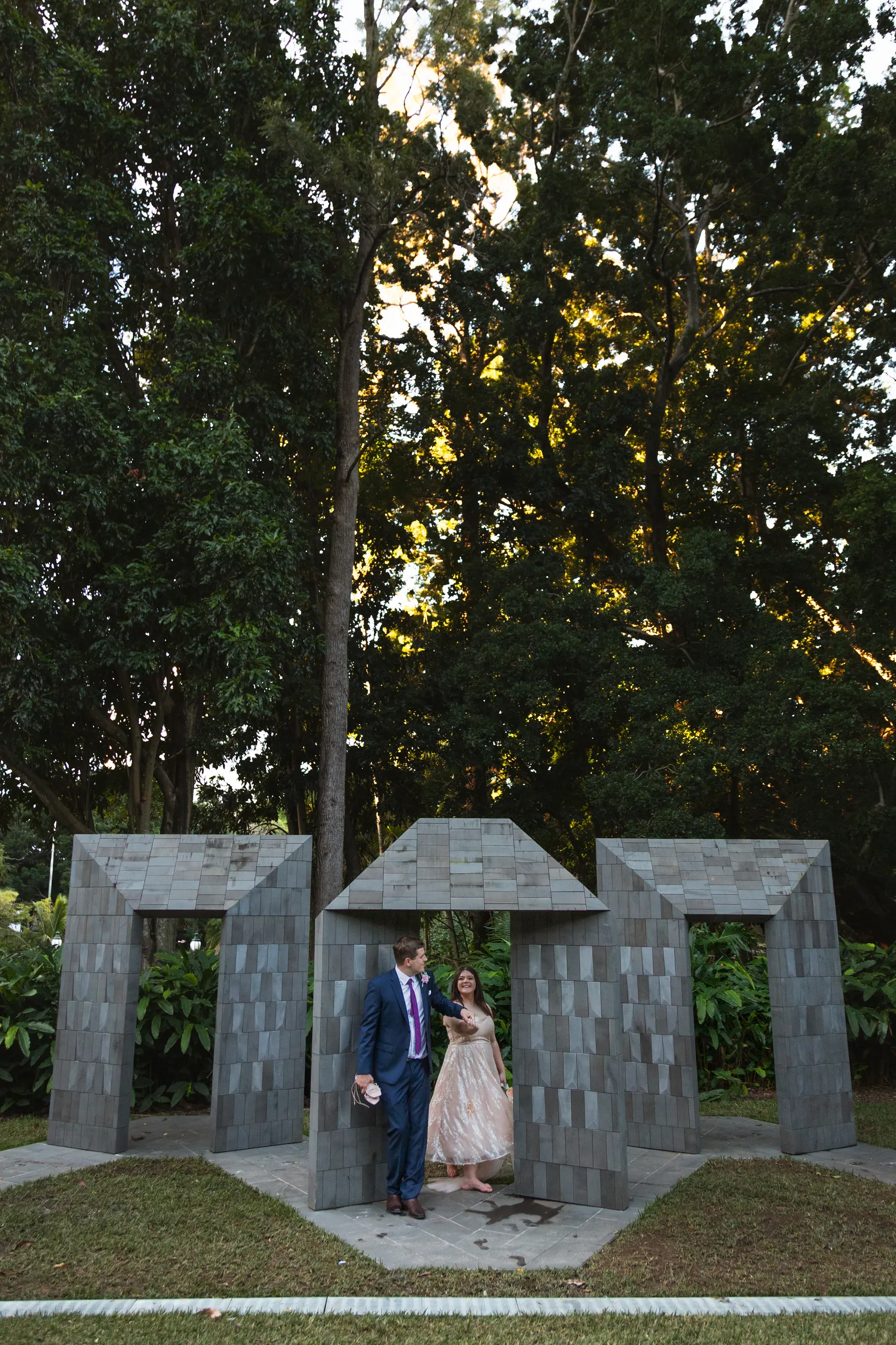 Carlie and Iain walking together through geometric stone archway structure with natural lighting