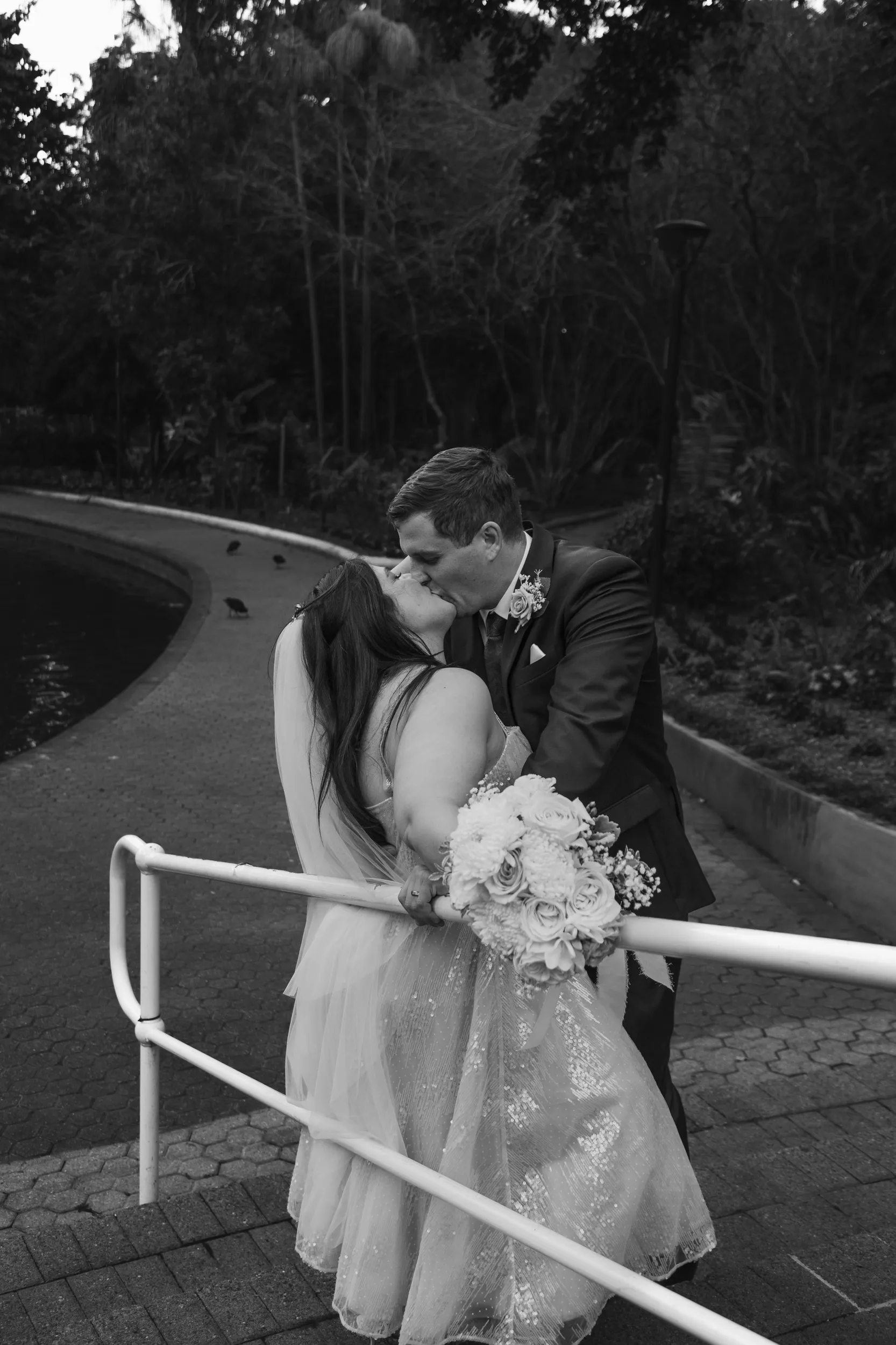 Carlie and Iain romantic black and white kiss on curved walkway with white railings and beautiful bouquet