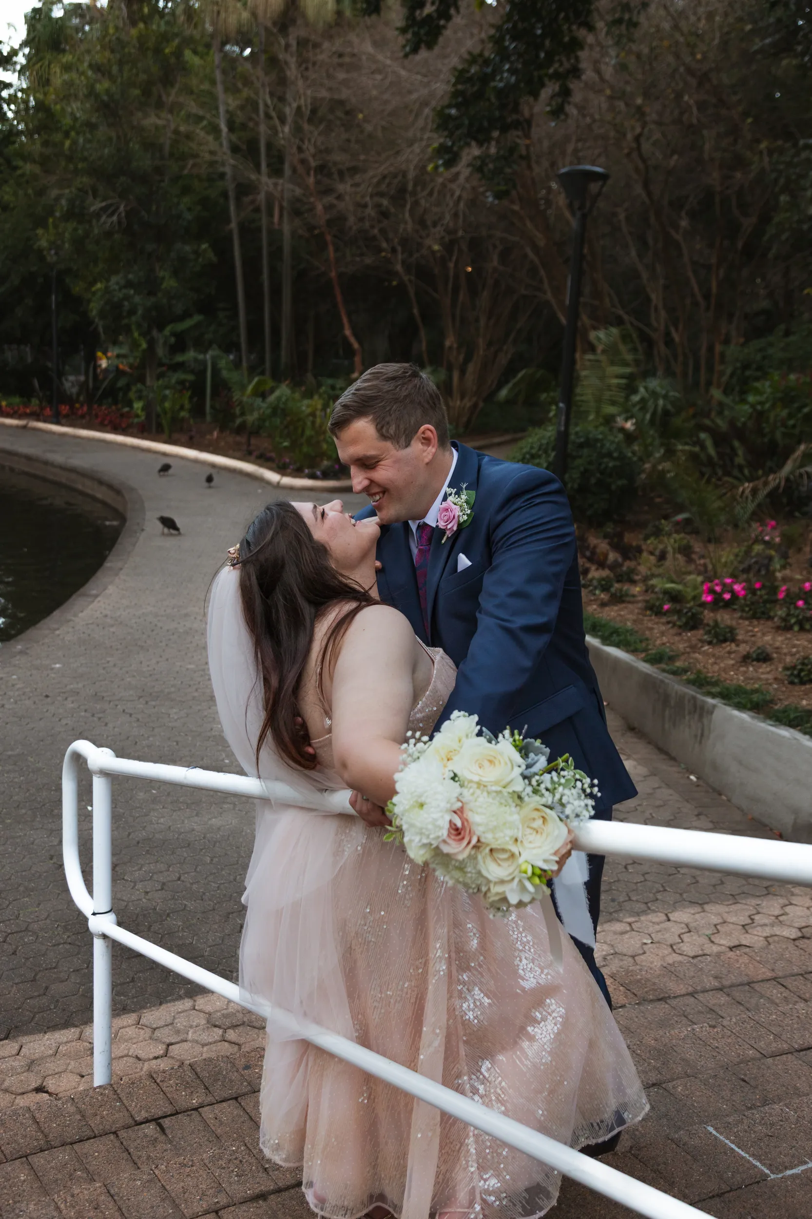 Carlie and Iain joyful moment laughing together on curved walkway in urban park with city buildings