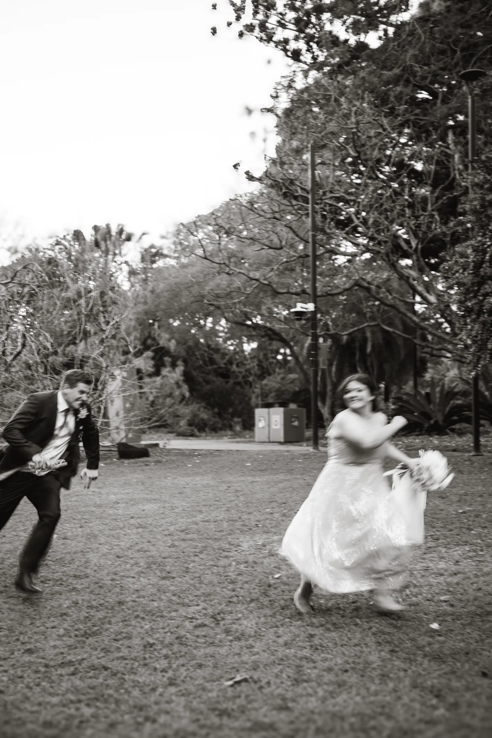 Carlie and Iain dynamic black and white action shot running together joyfully in park setting