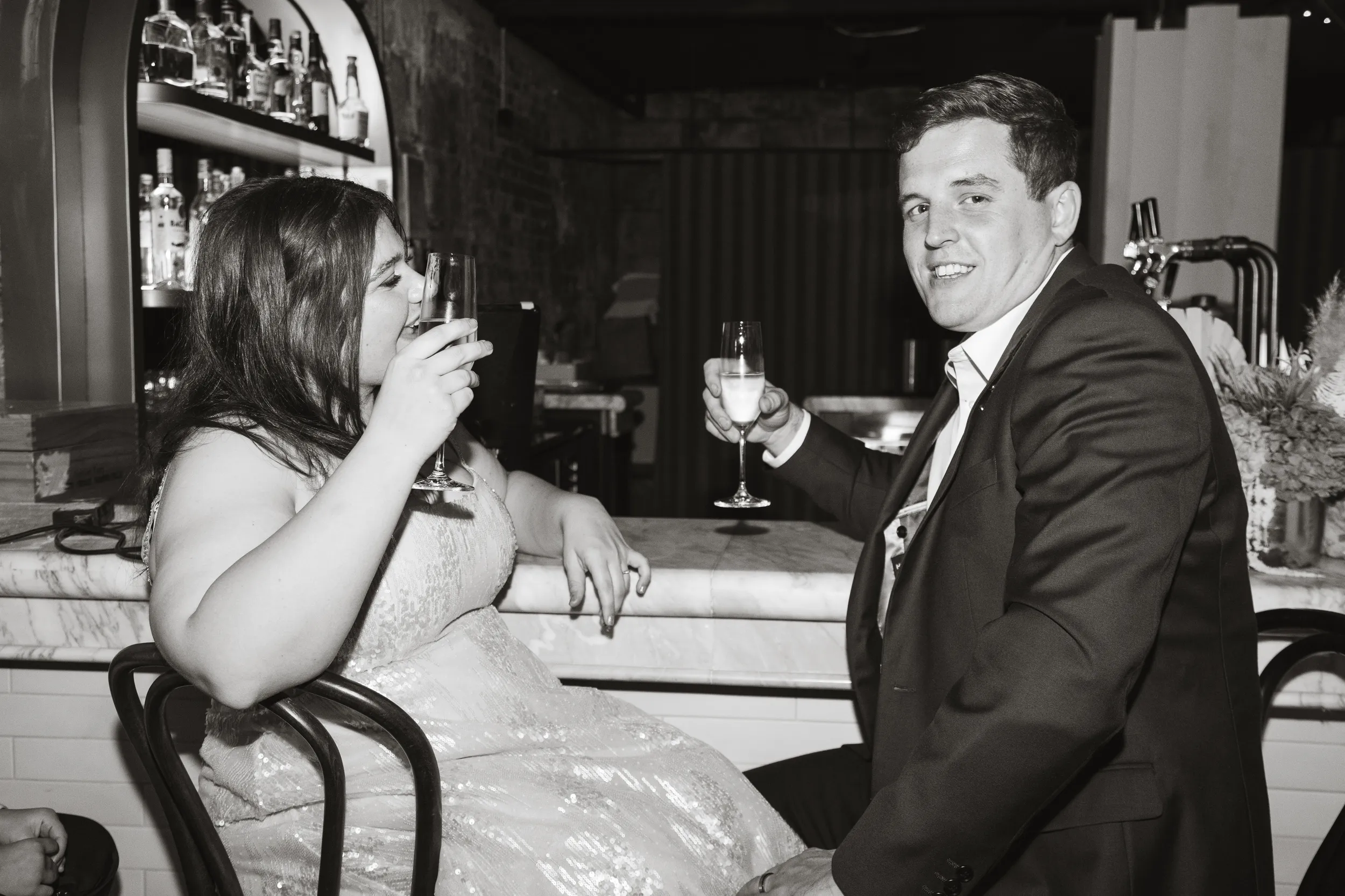 Carlie and Iain black and white toasting moment at bar with drinks during wedding celebration