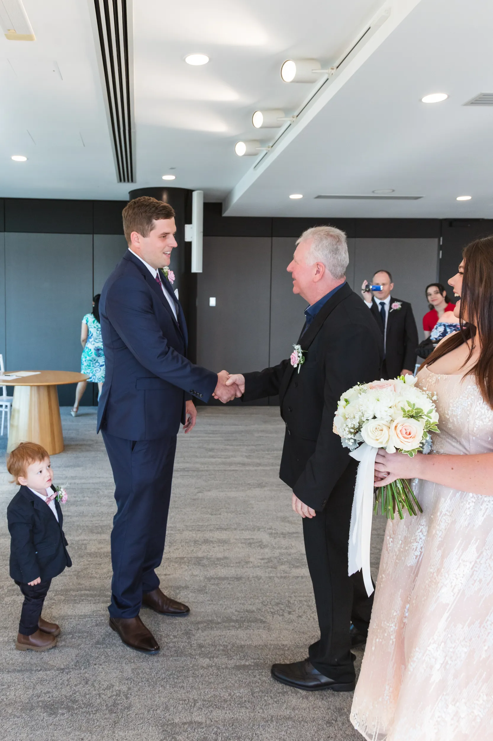Iain formal ceremony handshake with bride's father in modern venue with family watching
