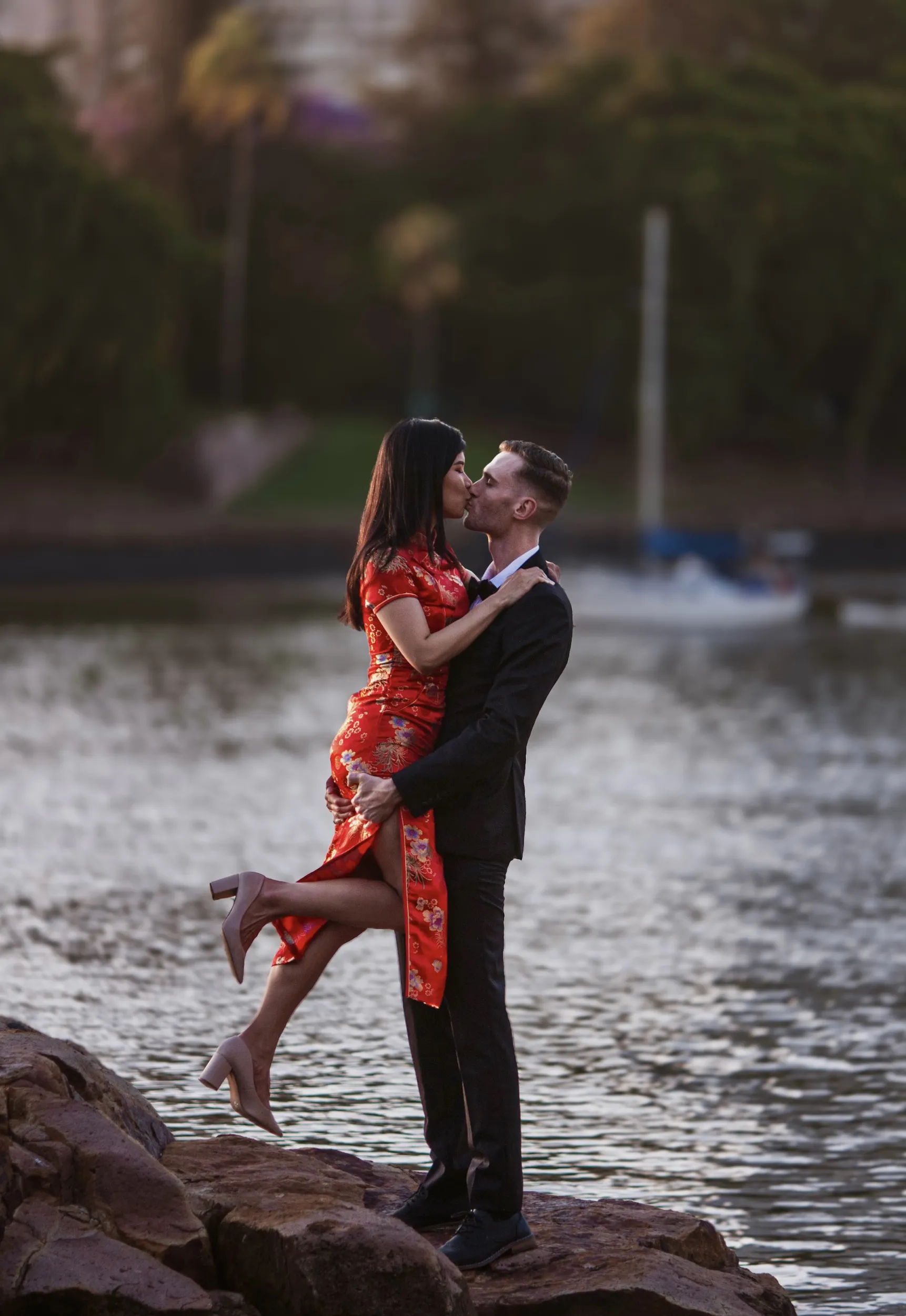 Romantic engagement photo of couple kissing by waterfront with woman in red traditional dress