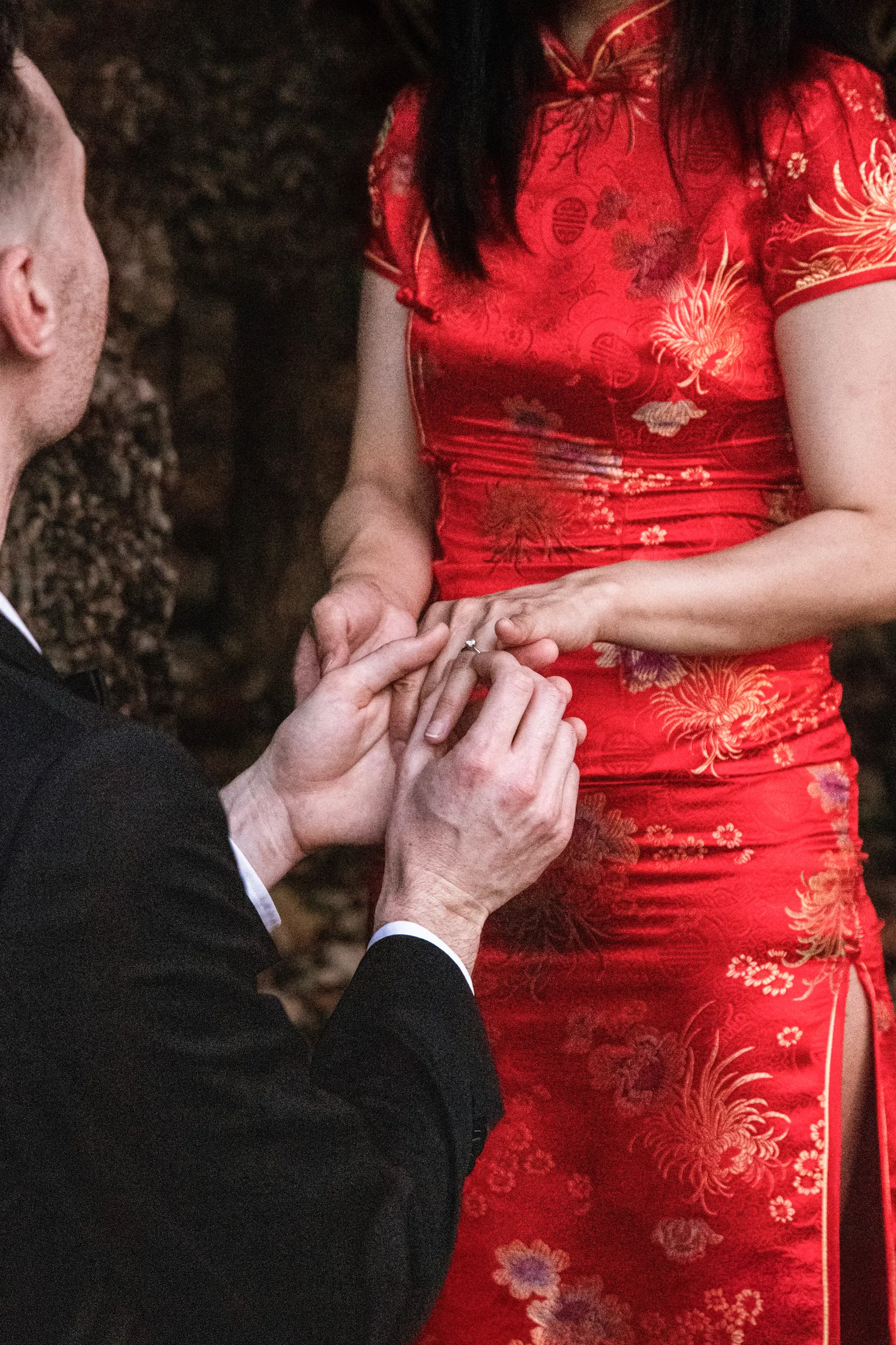 Artistic detail shot of hands during ring exchange with woman in red traditional dress