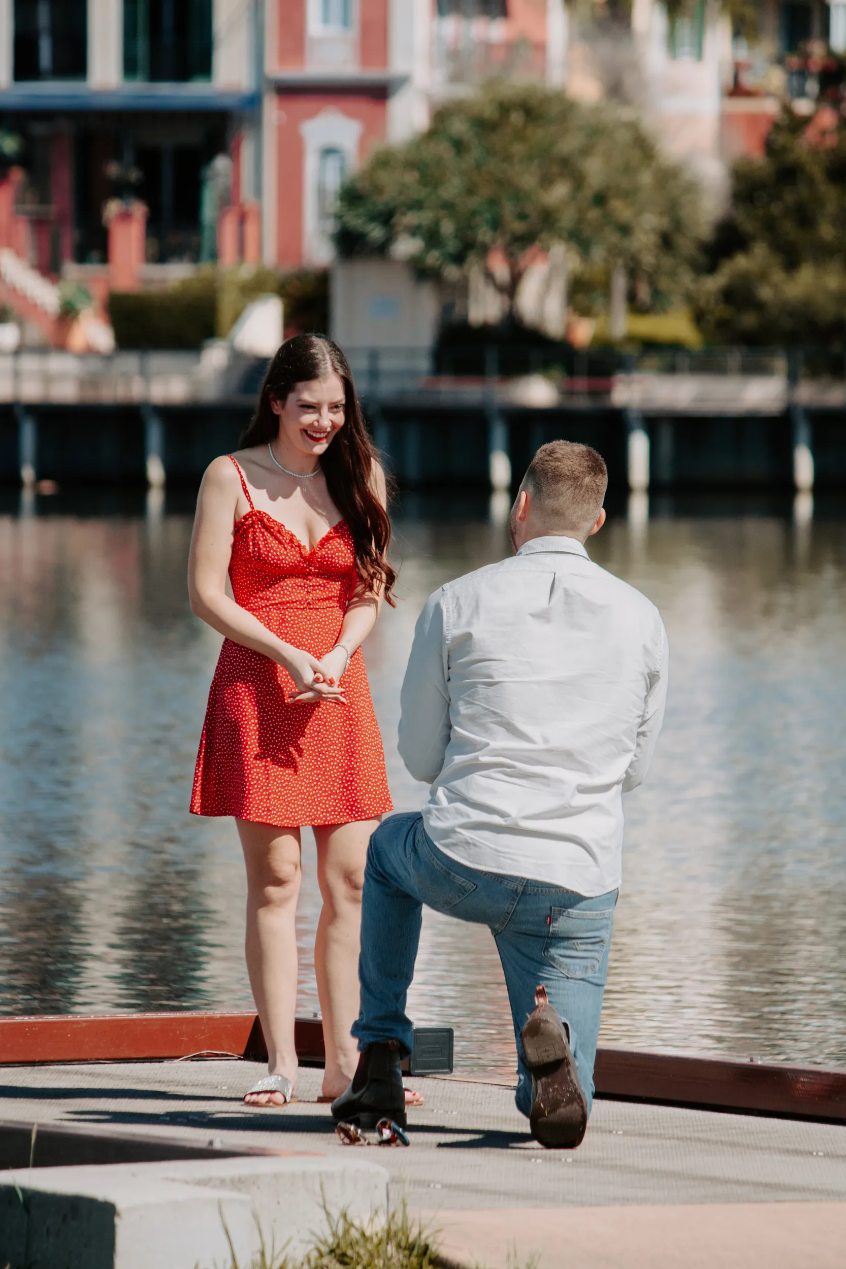 Bright daytime marriage proposal by colorful waterfront buildings with man kneeling