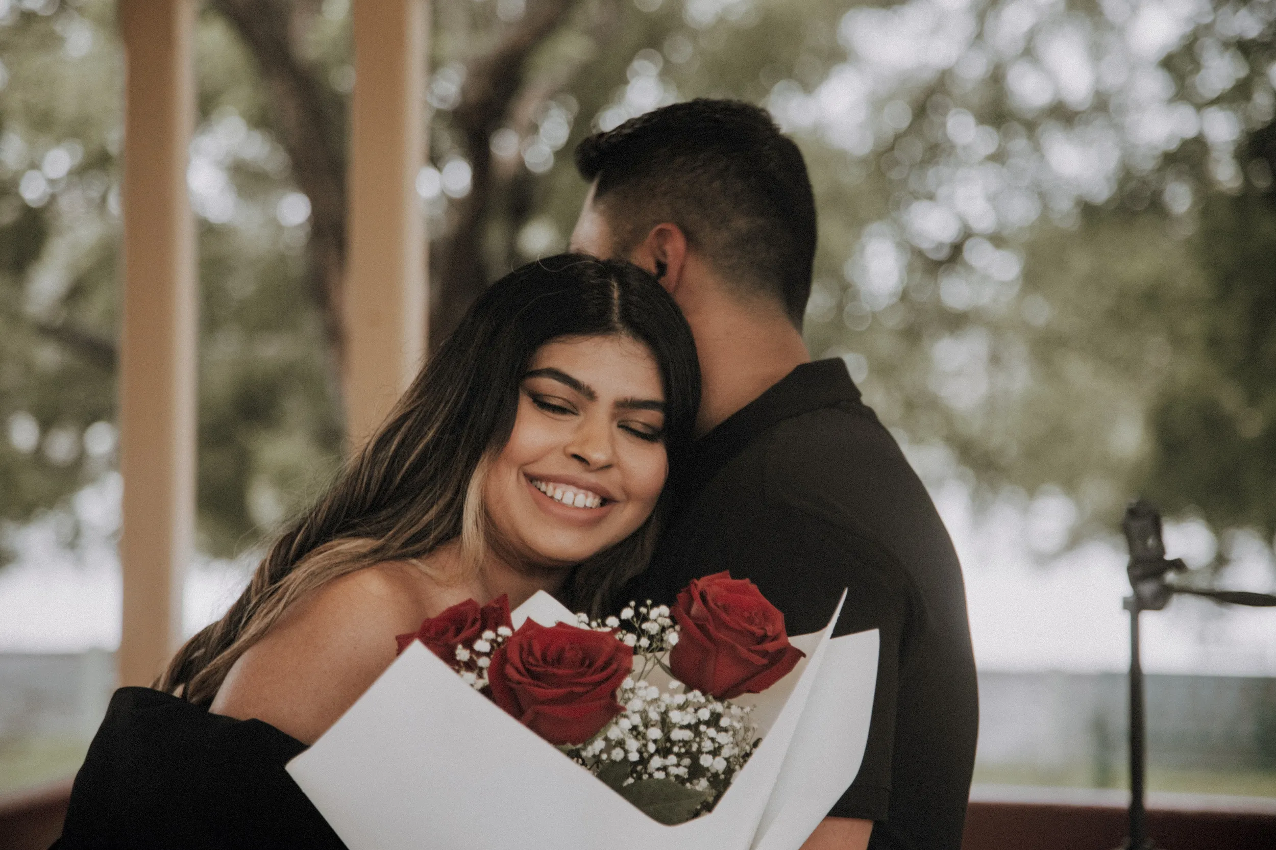 Sweet engagement photo with red roses bouquet and couple embracing in natural light