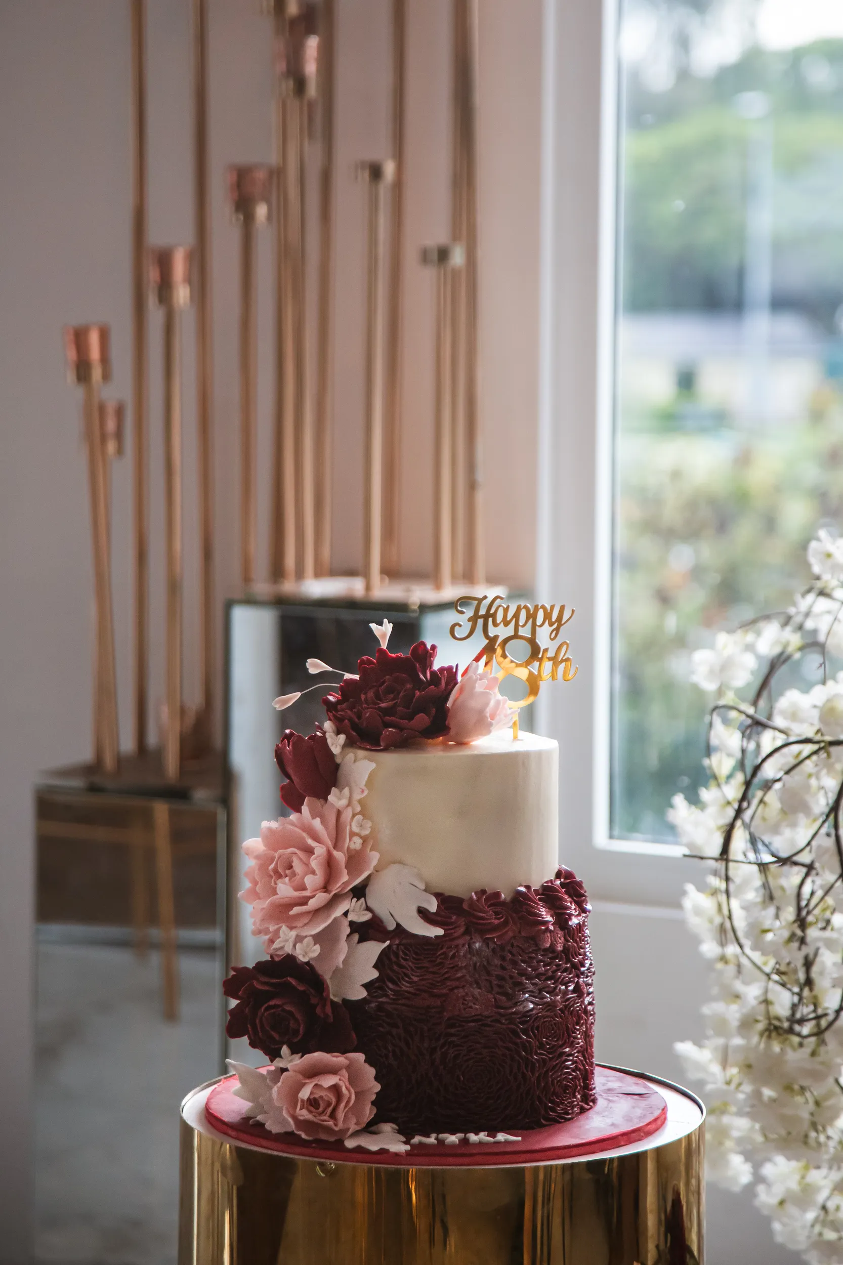Elegant two-tier 18th birthday cake with Happy 18th golden topper and burgundy roses on gold pedestal