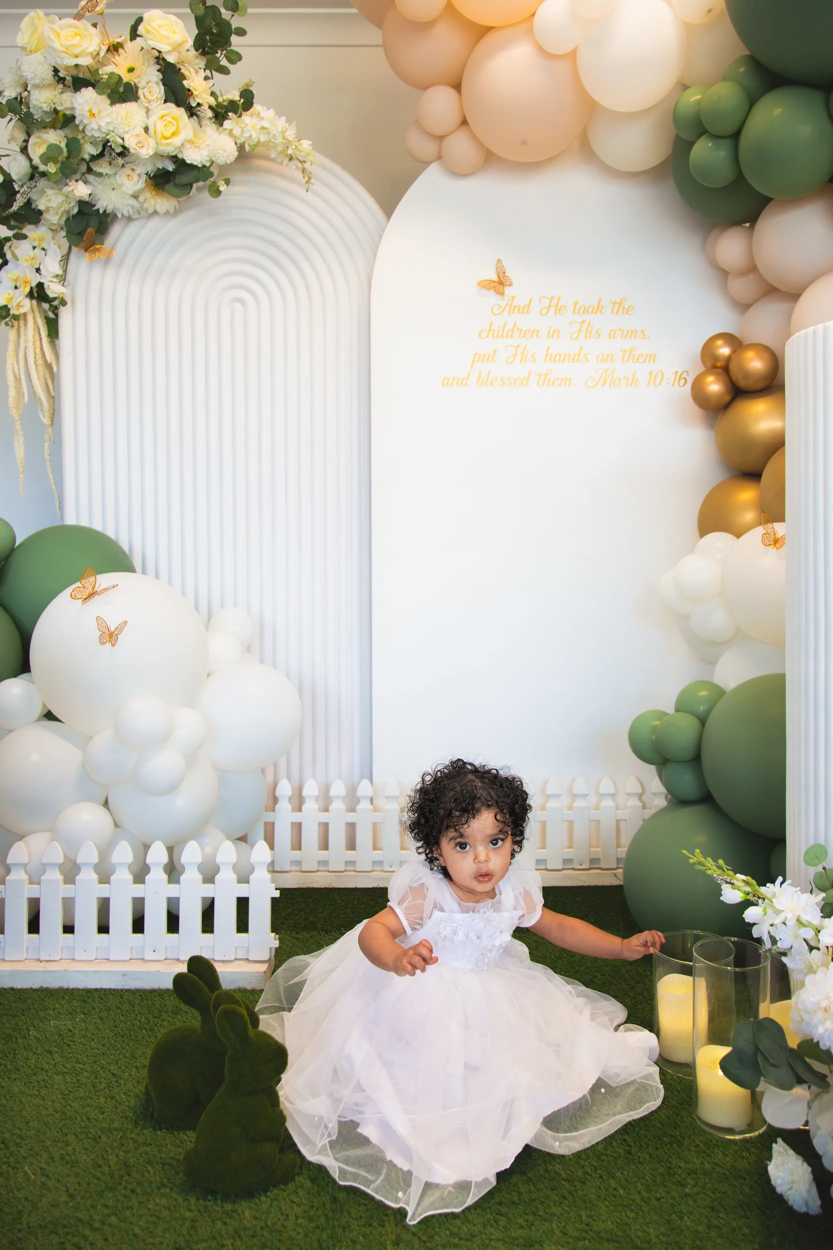 Beautiful baptism setup with child in white dress, balloon arch, and biblical quote decoration