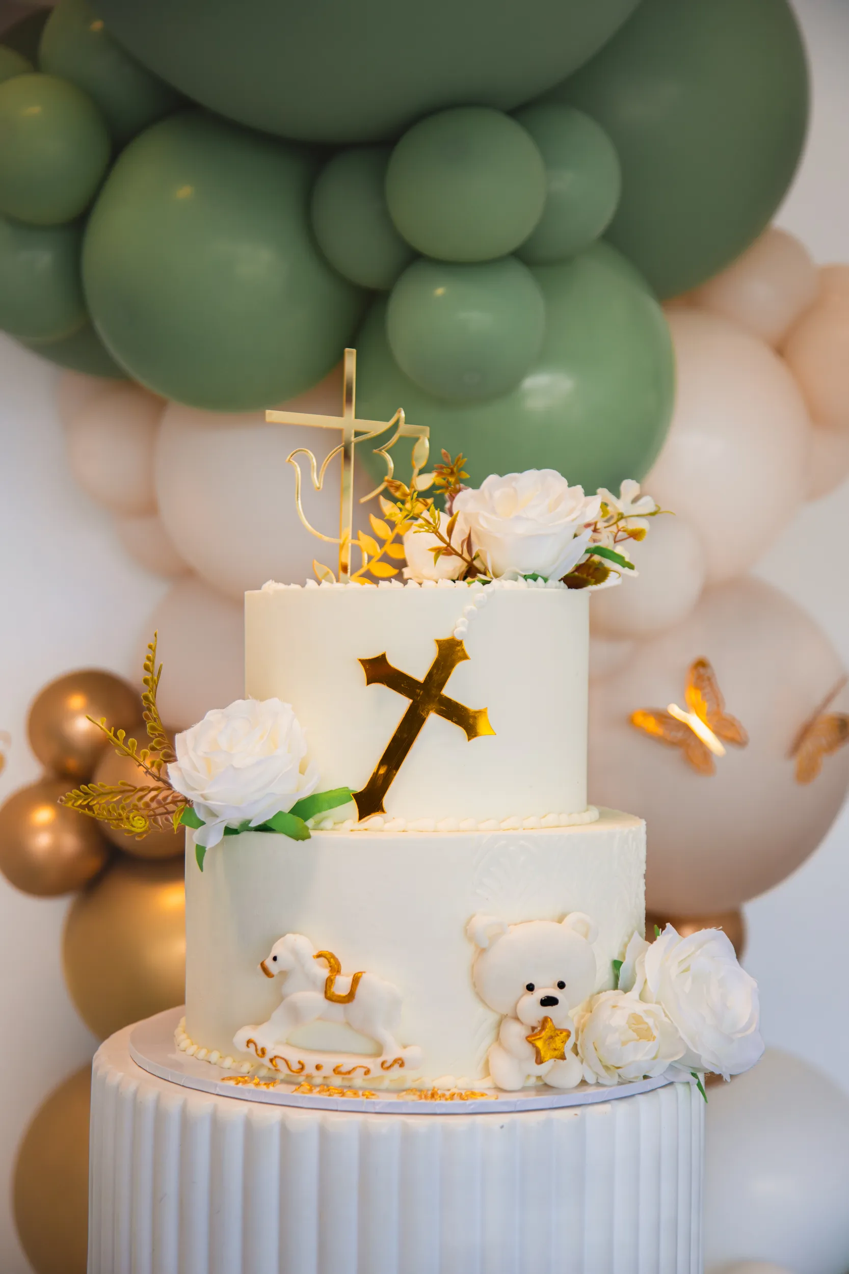 Stunning two-tier baptism cake with golden cross, white roses, and adorable lamb and teddy bear decorations