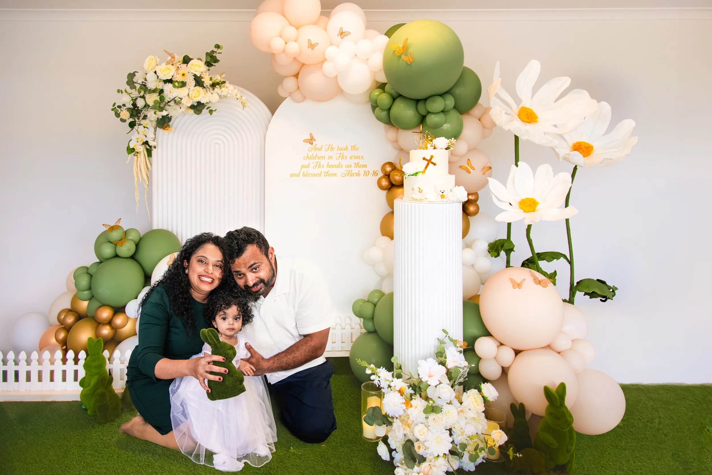 Beautiful baptism family portrait with parents and child in front of elaborate balloon arch setup