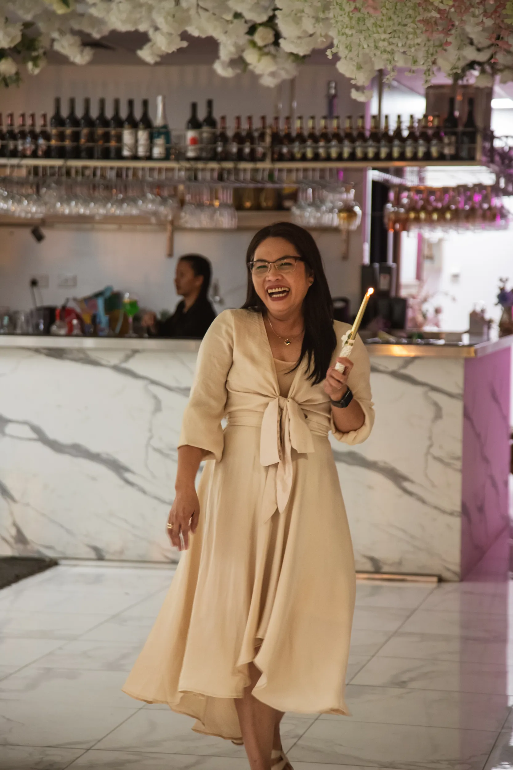 Joyful celebration moment with woman in beige dress holding sparkler at elegant marble bar venue