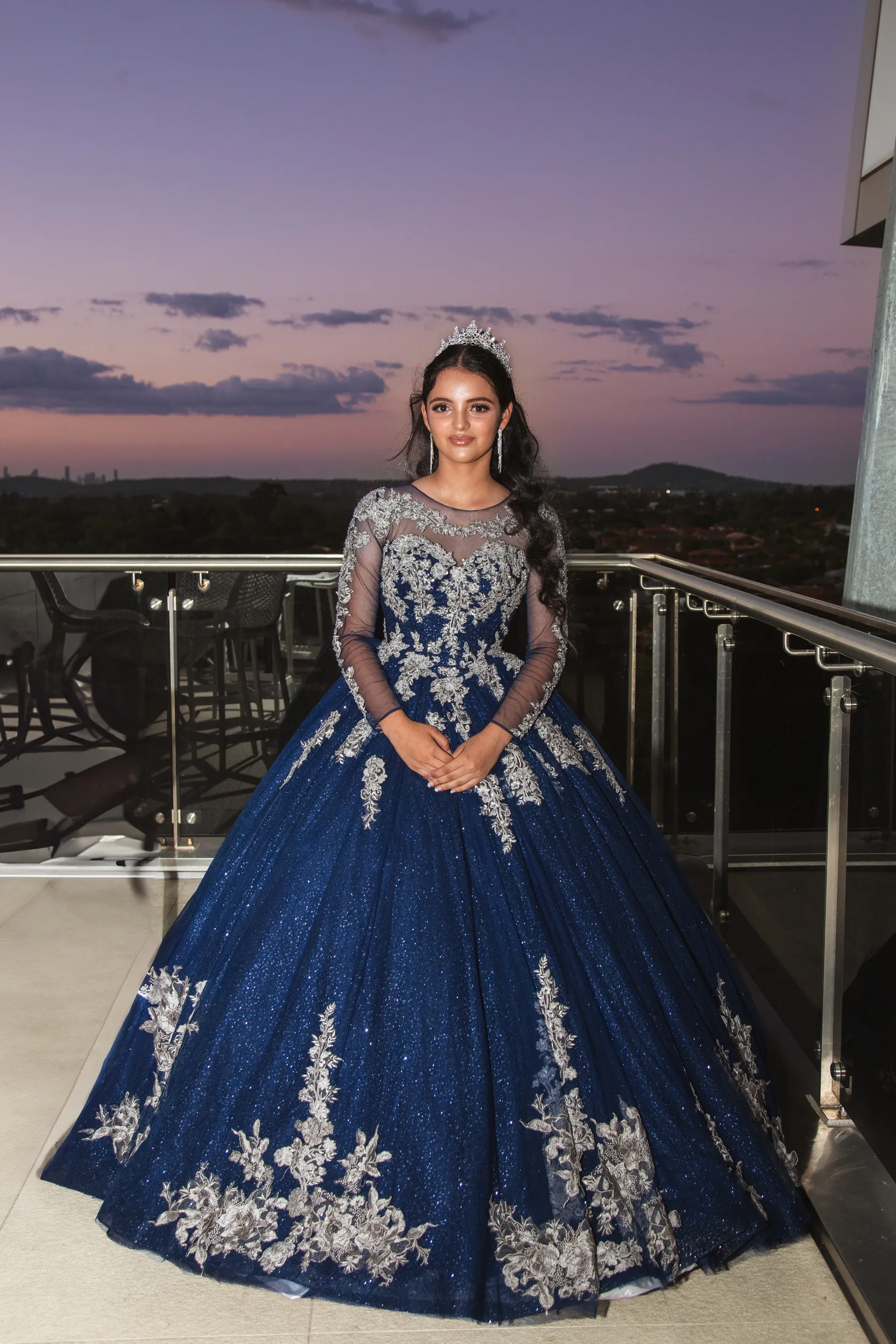 Breathtaking debut portrait in elaborate blue ball gown with tiara on balcony during purple sunset