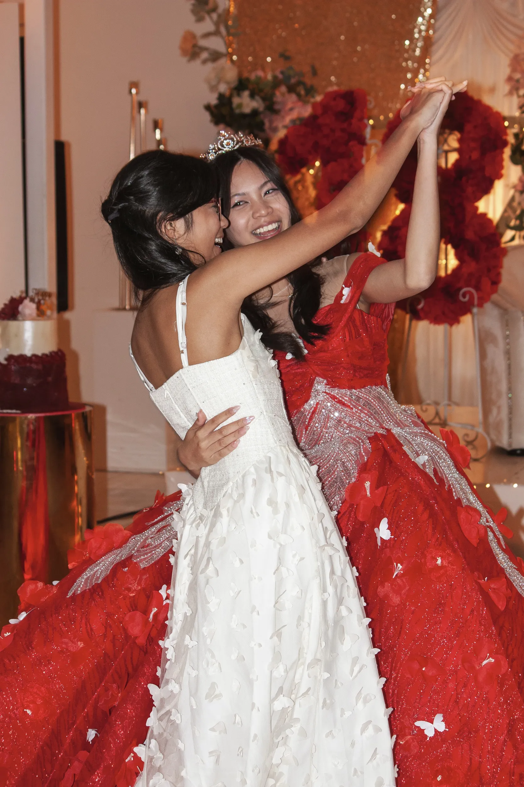 Joyful debut celebration with two young women embracing, one in red ball gown with tiara
