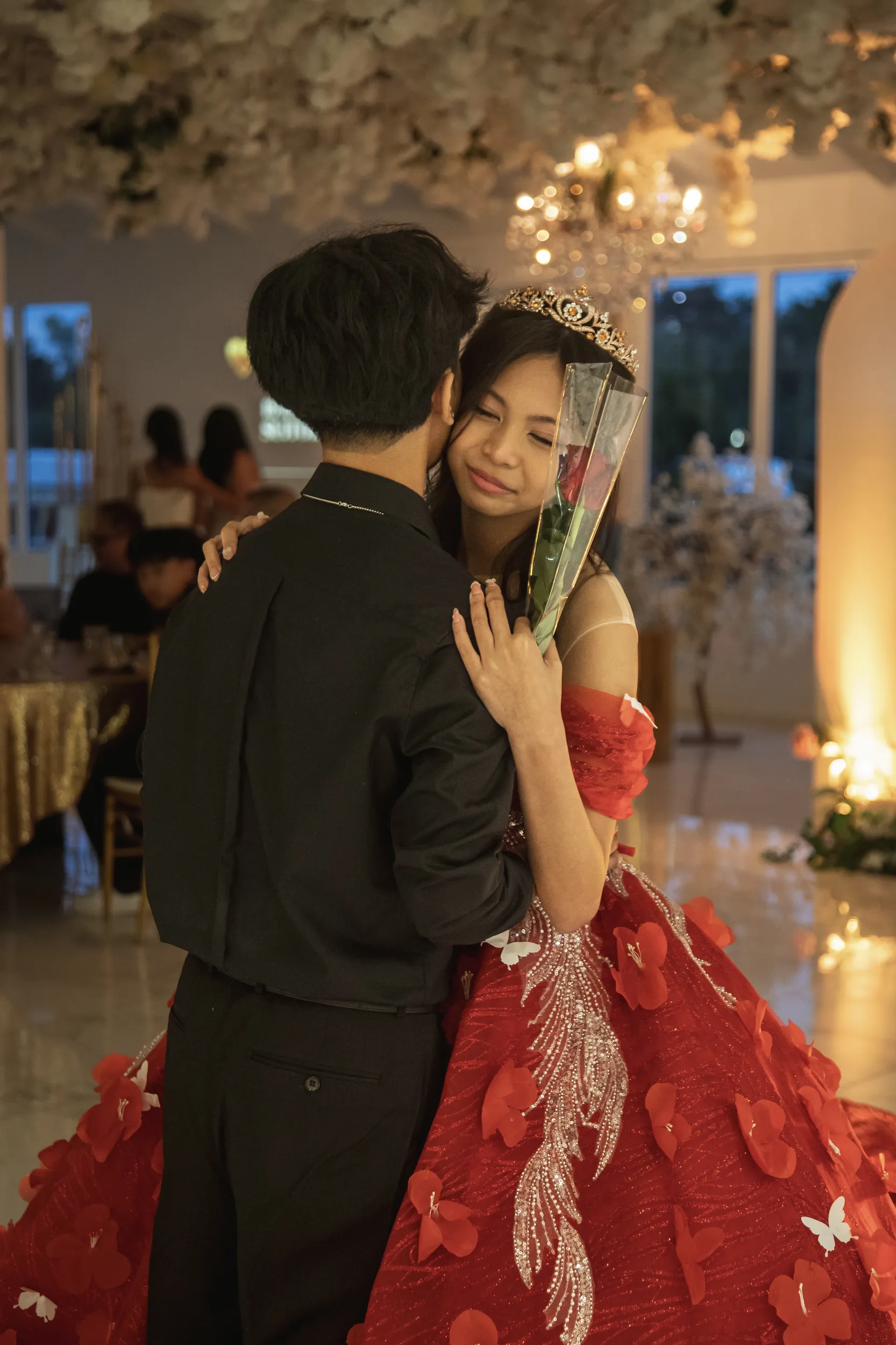 Touching debut moment with young woman in red ball gown and tiara embracing man with single rose