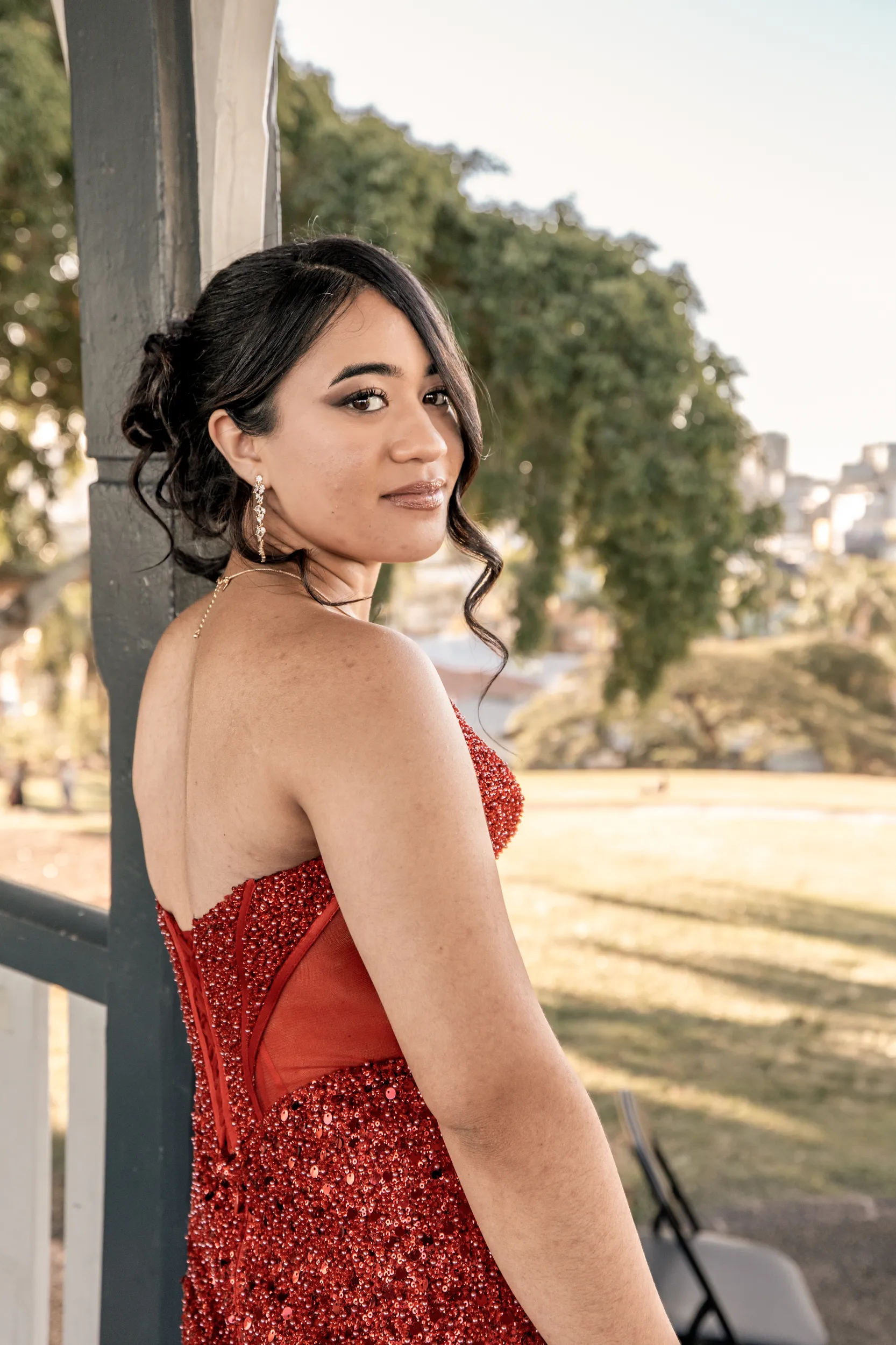 Elegant debut portrait of young woman in red sparkly dress during golden hour on porch