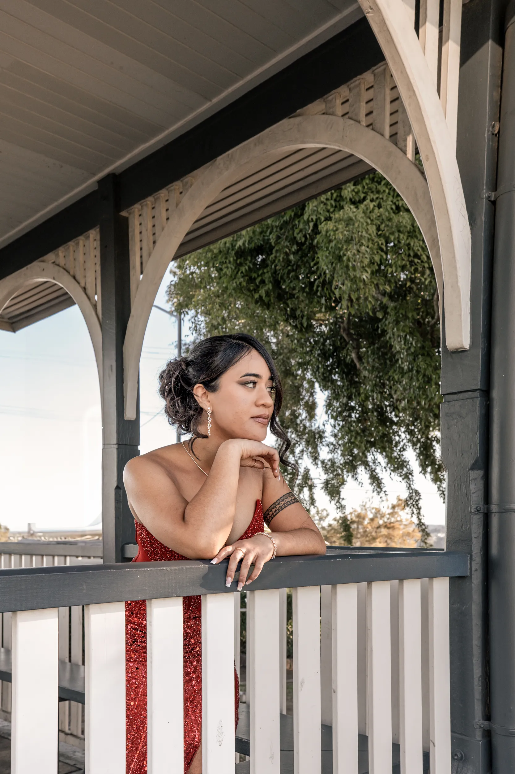 Elegant debut portrait of young woman in red sparkly dress on covered porch with natural lighting