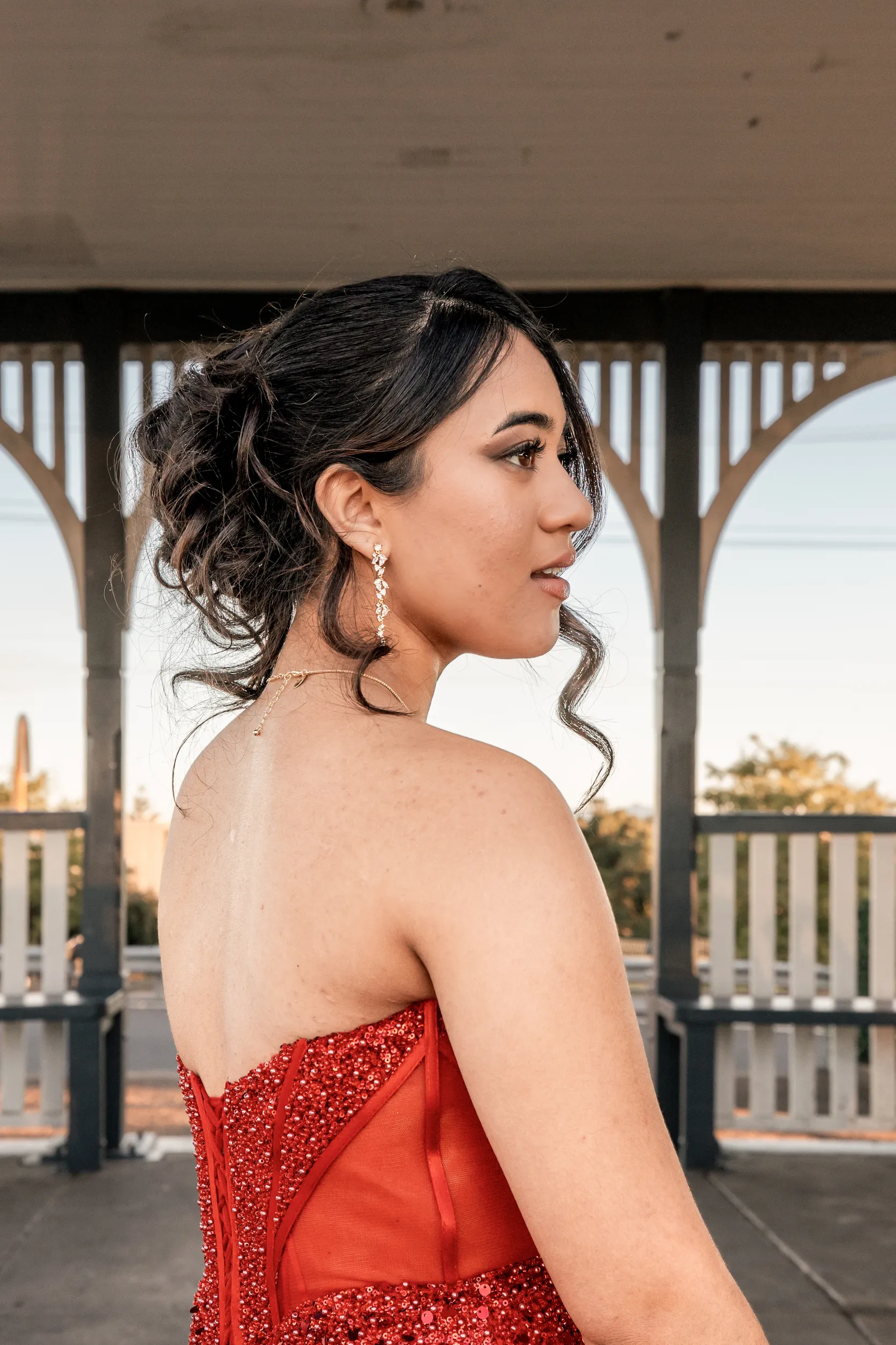 Elegant debut profile portrait in red sequined dress with drop earrings during golden hour