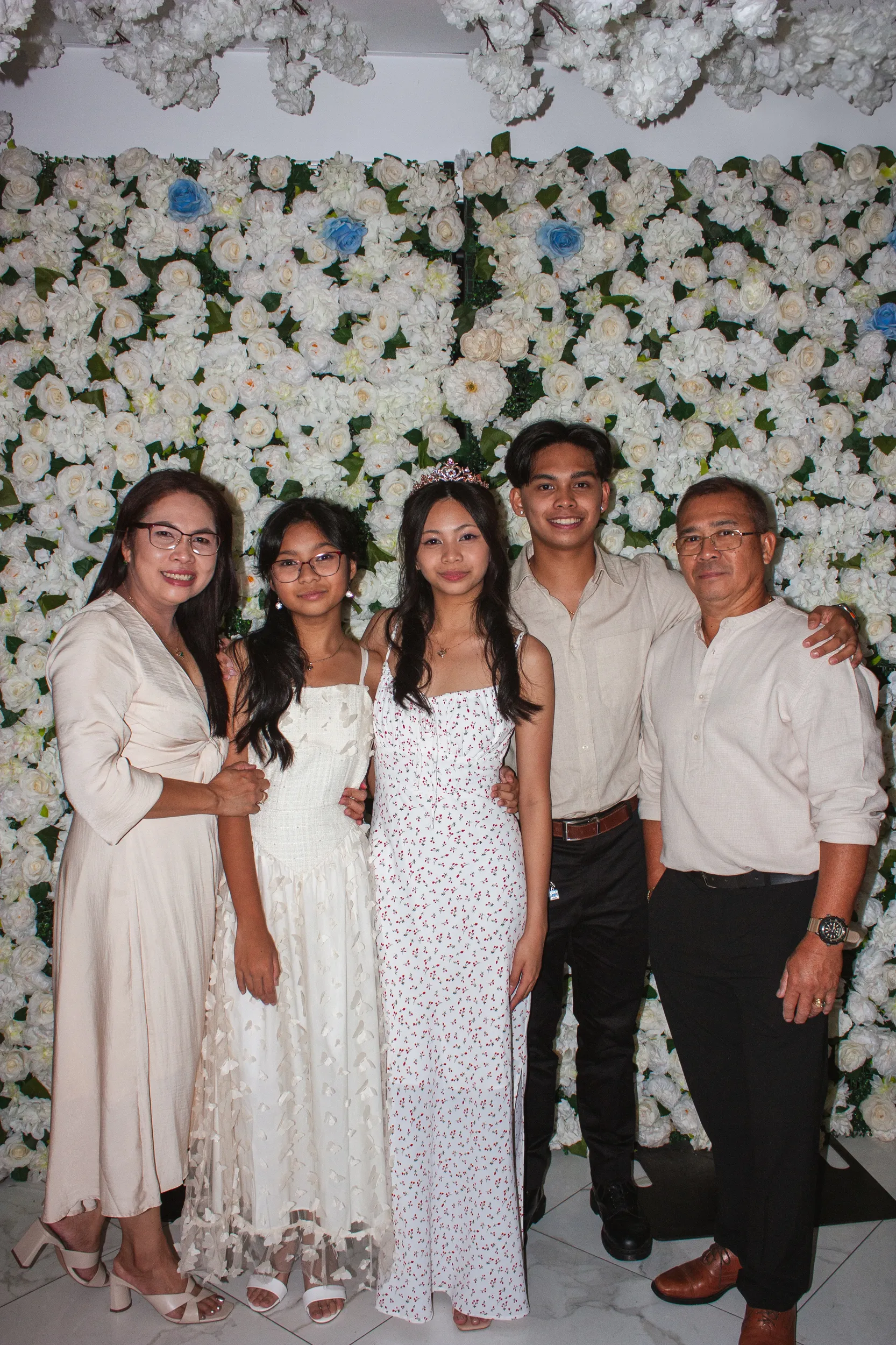 Family portrait of five people in front of white floral wall at debut celebration