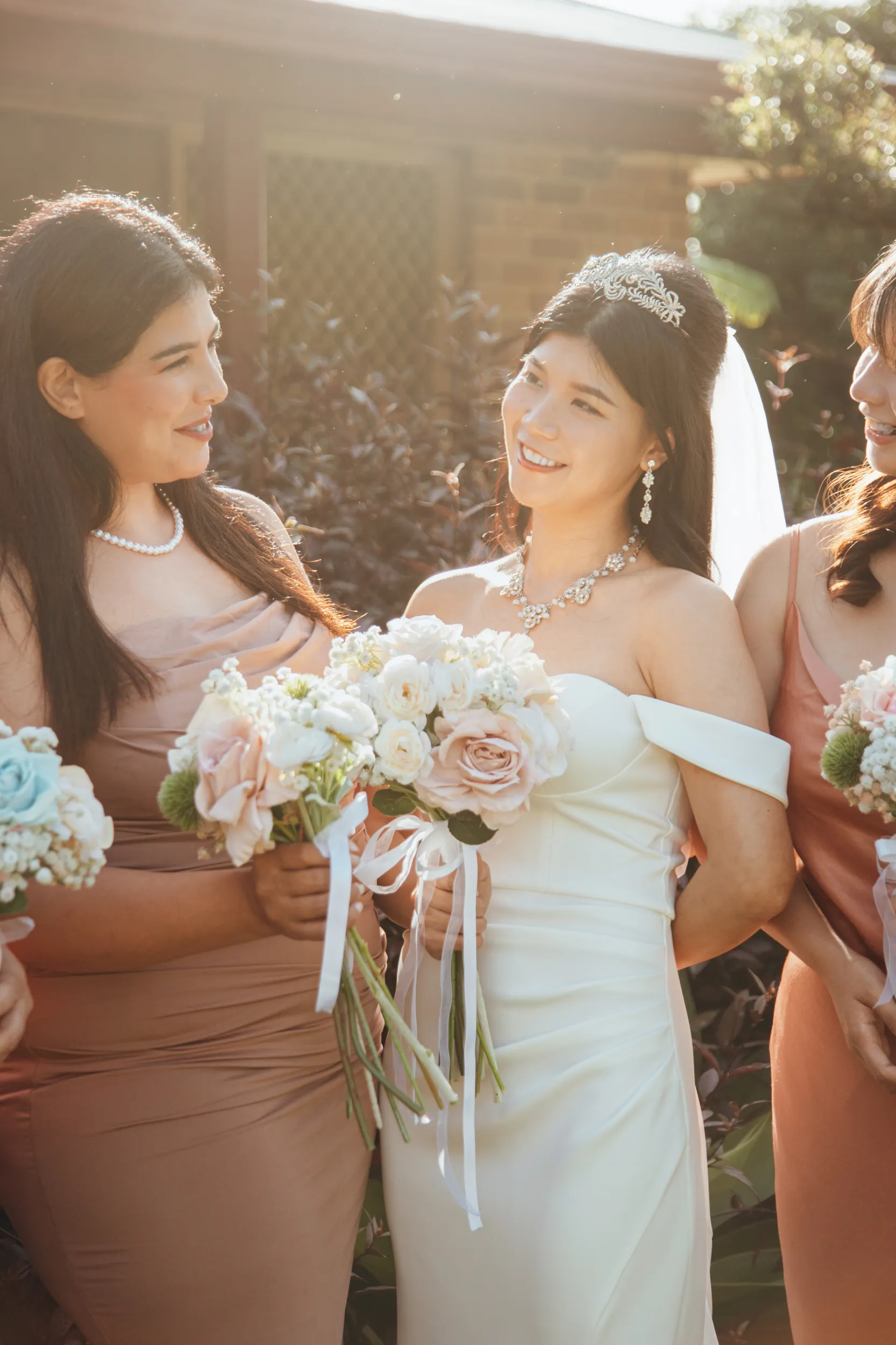 Huiyu with bridesmaids in golden hour lighting, bride wearing crystal tiara and statement necklace with white rose bouquets