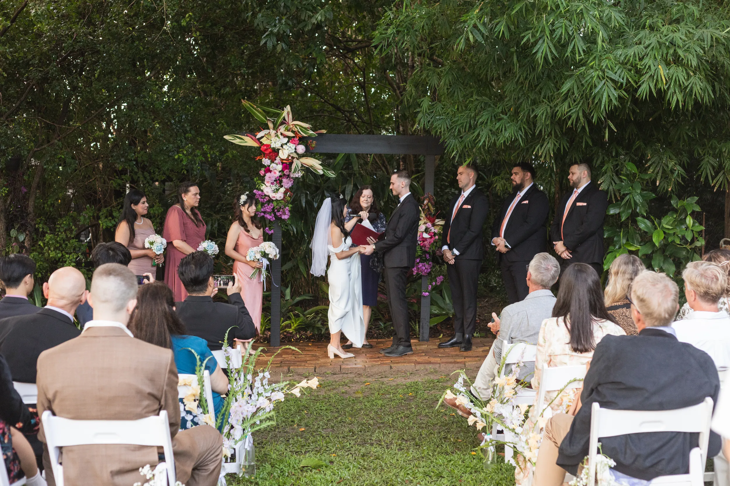 Huiyu and Chris wedding ceremony at altar under black arch with vibrant pink and purple flowers surrounded by guests