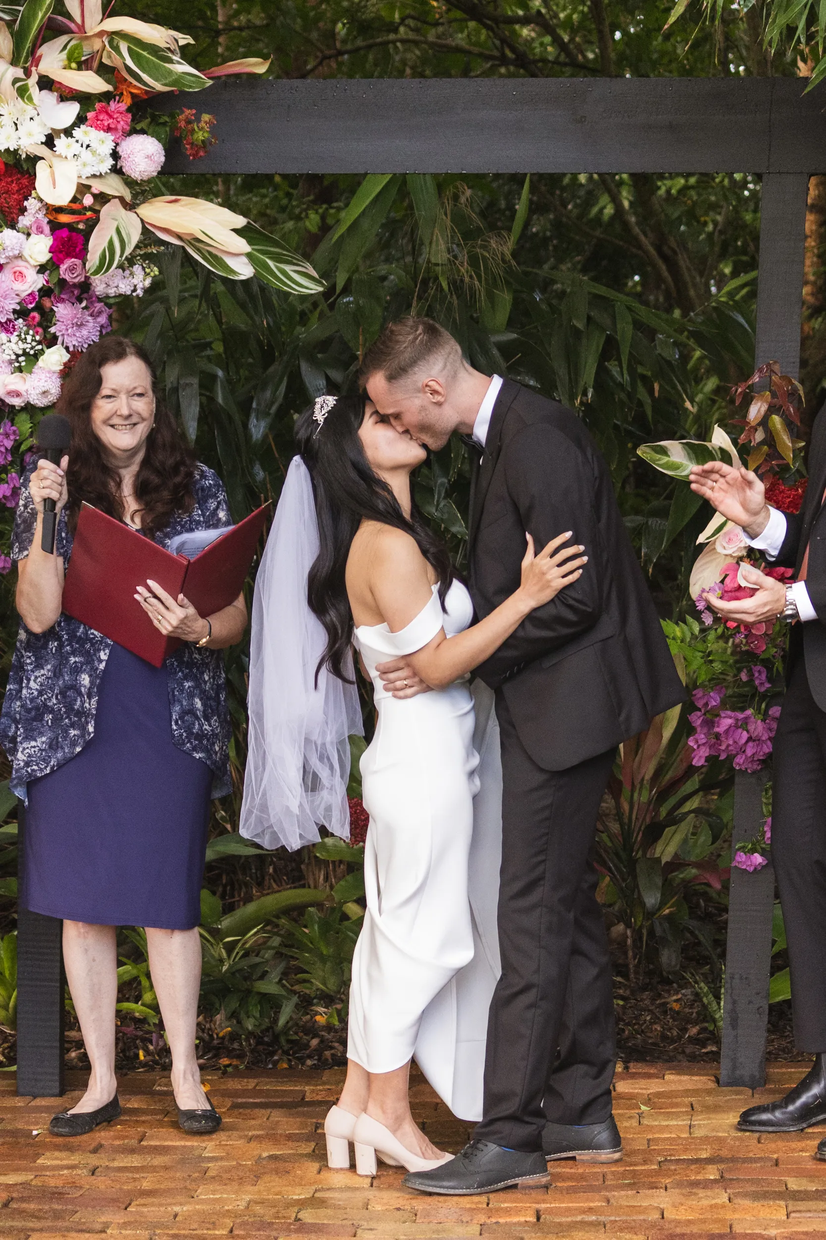 Huiyu and Chris first kiss under floral arch with female officiant and vibrant pink purple flowers