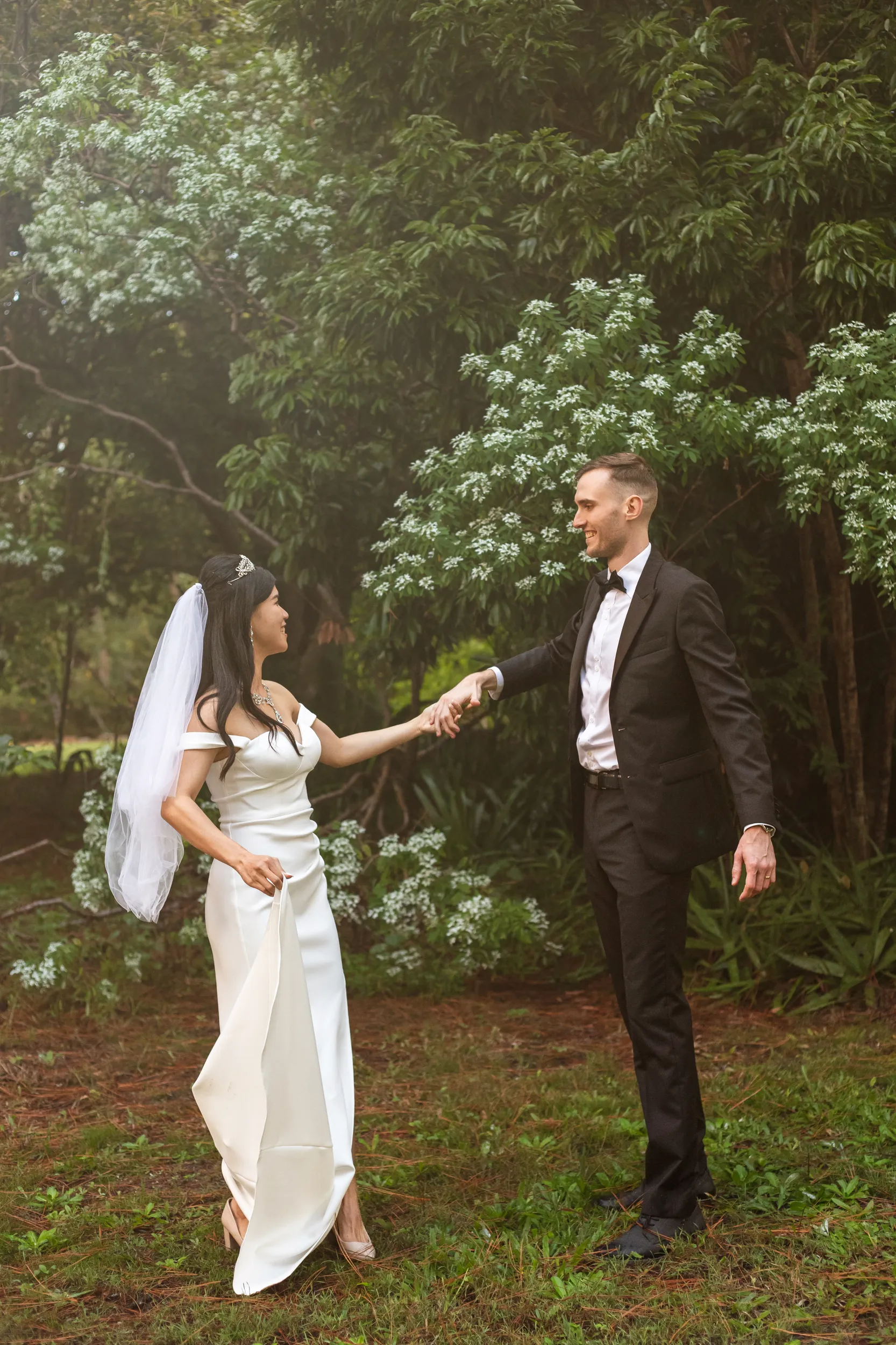 Huiyu and Chris joyful moment holding hands and dancing in garden with bride's dress flowing among white flowering trees