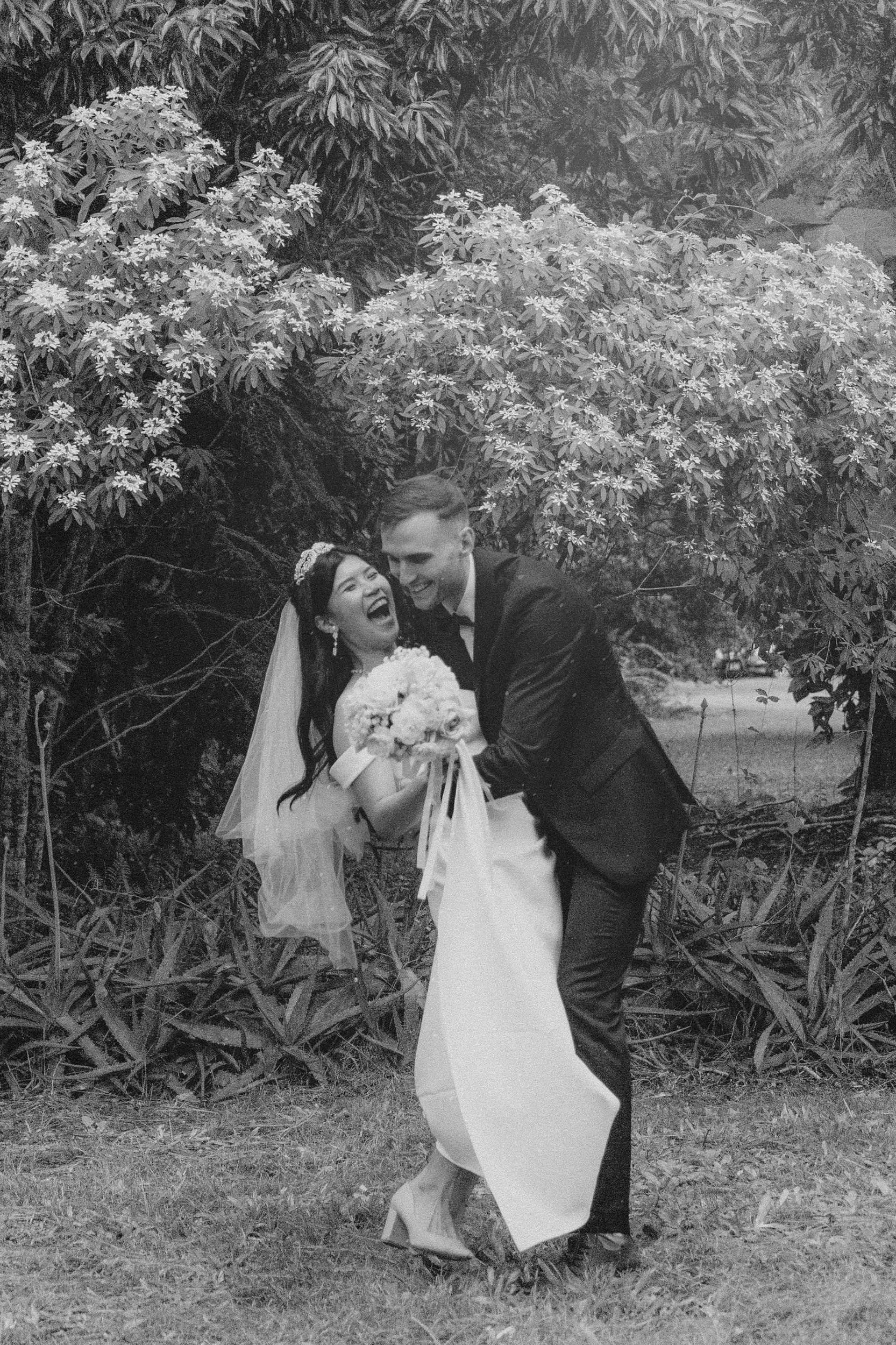 Huiyu and Chris artistic black and white photo laughing together in garden with bride holding bouquet