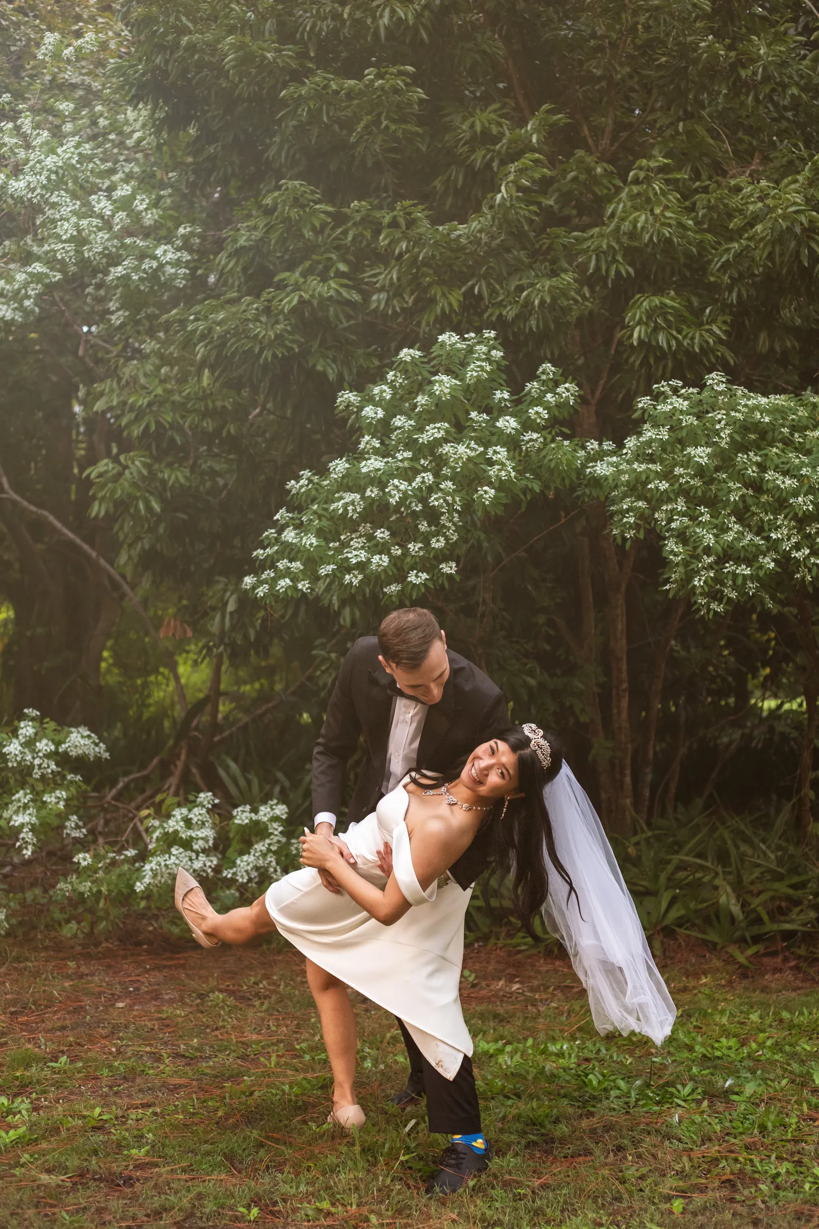 Huiyu and Chris dramatic romantic dip pose in garden with bride's dress flowing against white flowering bushes