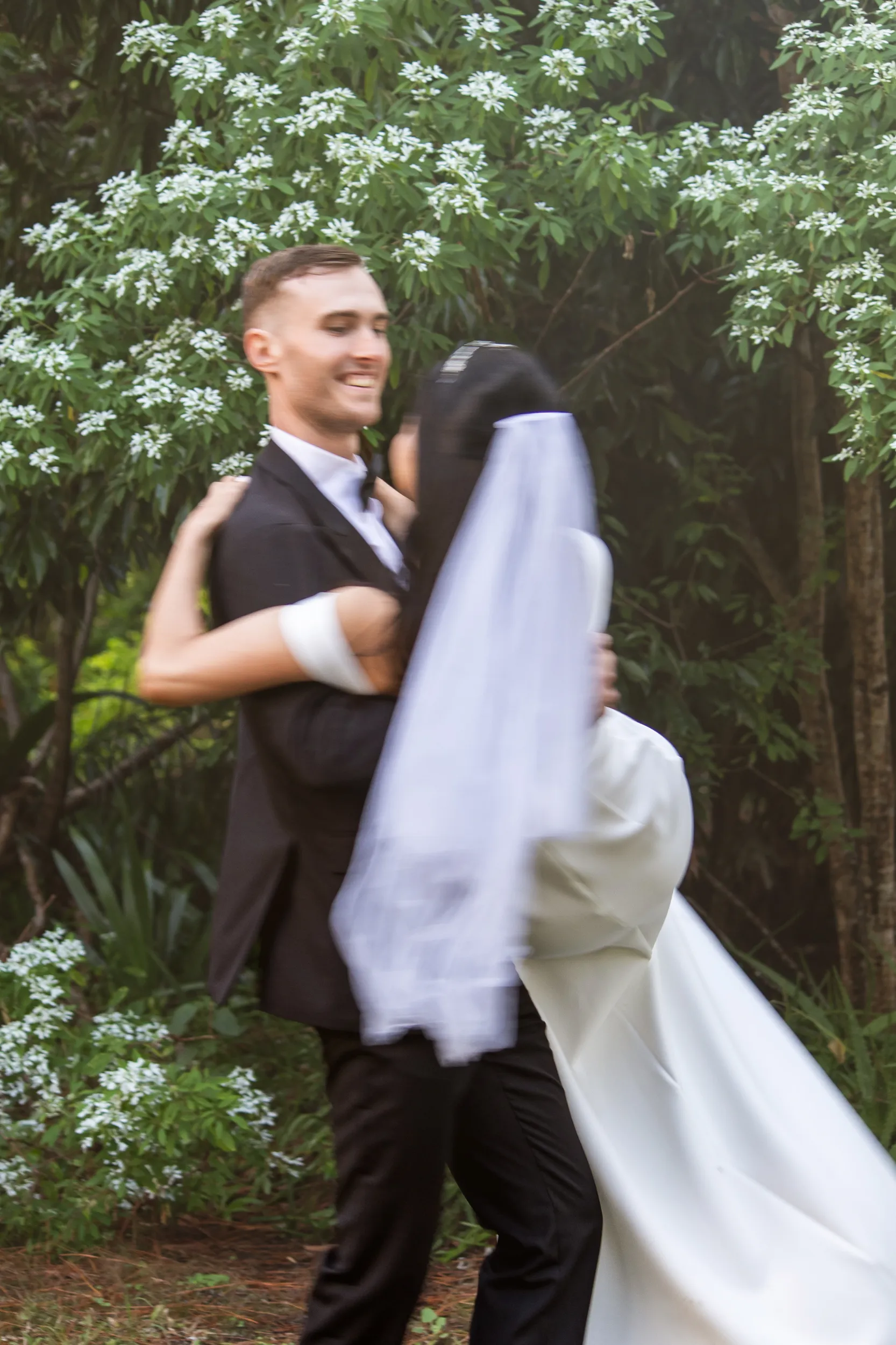 Huiyu and Chris romantic moment with groom spinning bride in garden with white flowering bushes