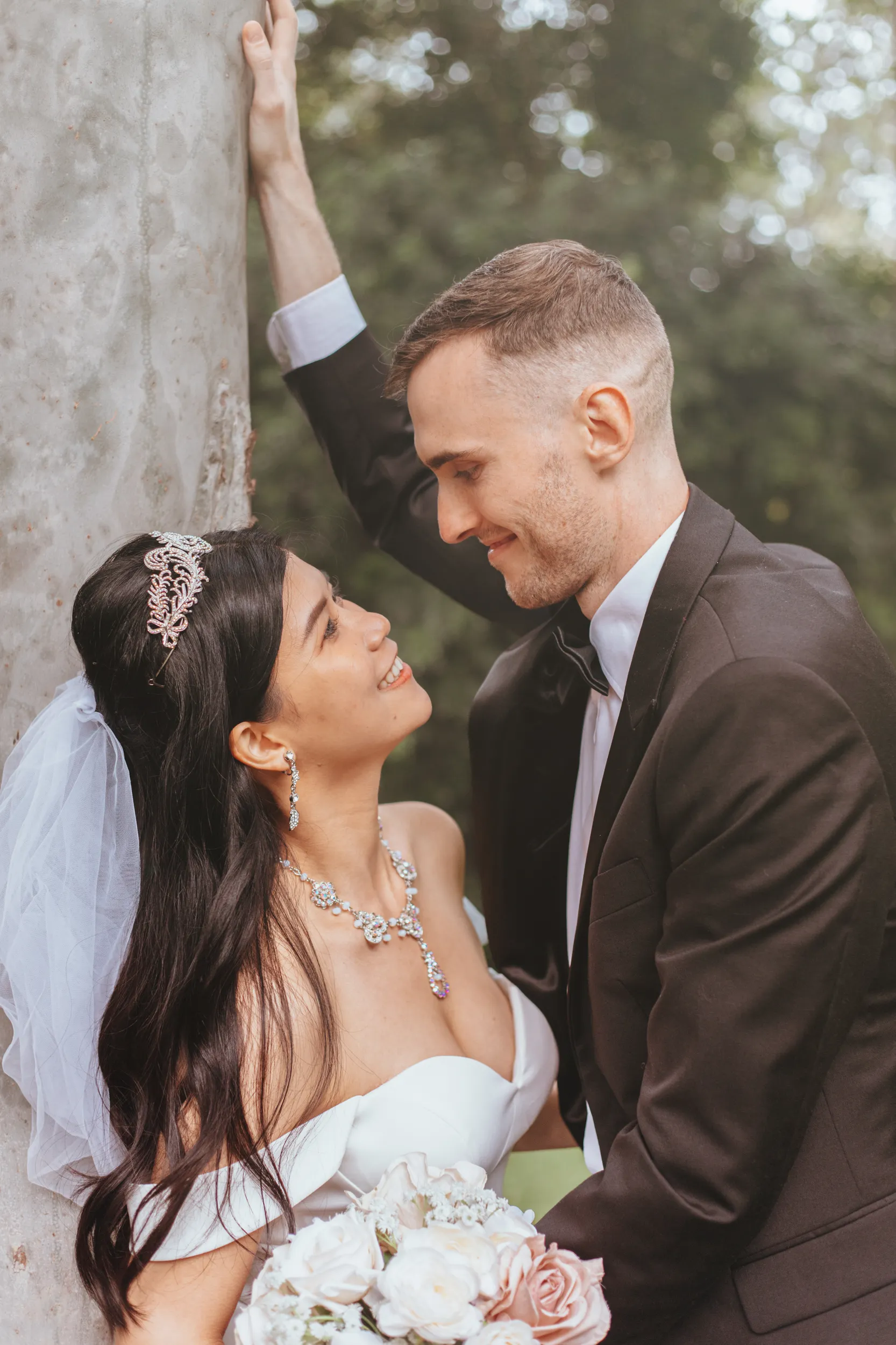Huiyu and Chris romantic portrait against tree with bride wearing crystal tiara and statement necklace in natural garden lighting