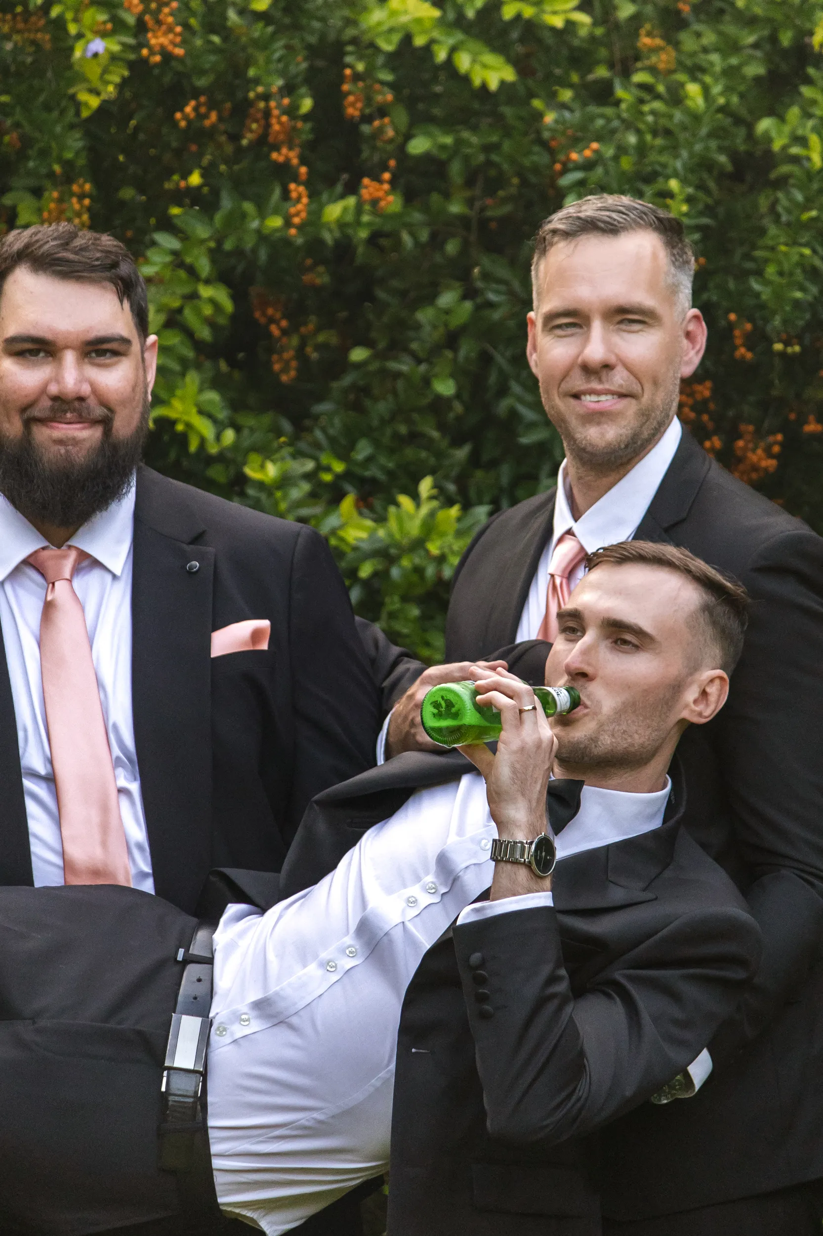 Chris and groomsmen candid moment relaxing with one drinking beer, all wearing dark suits with pink ties