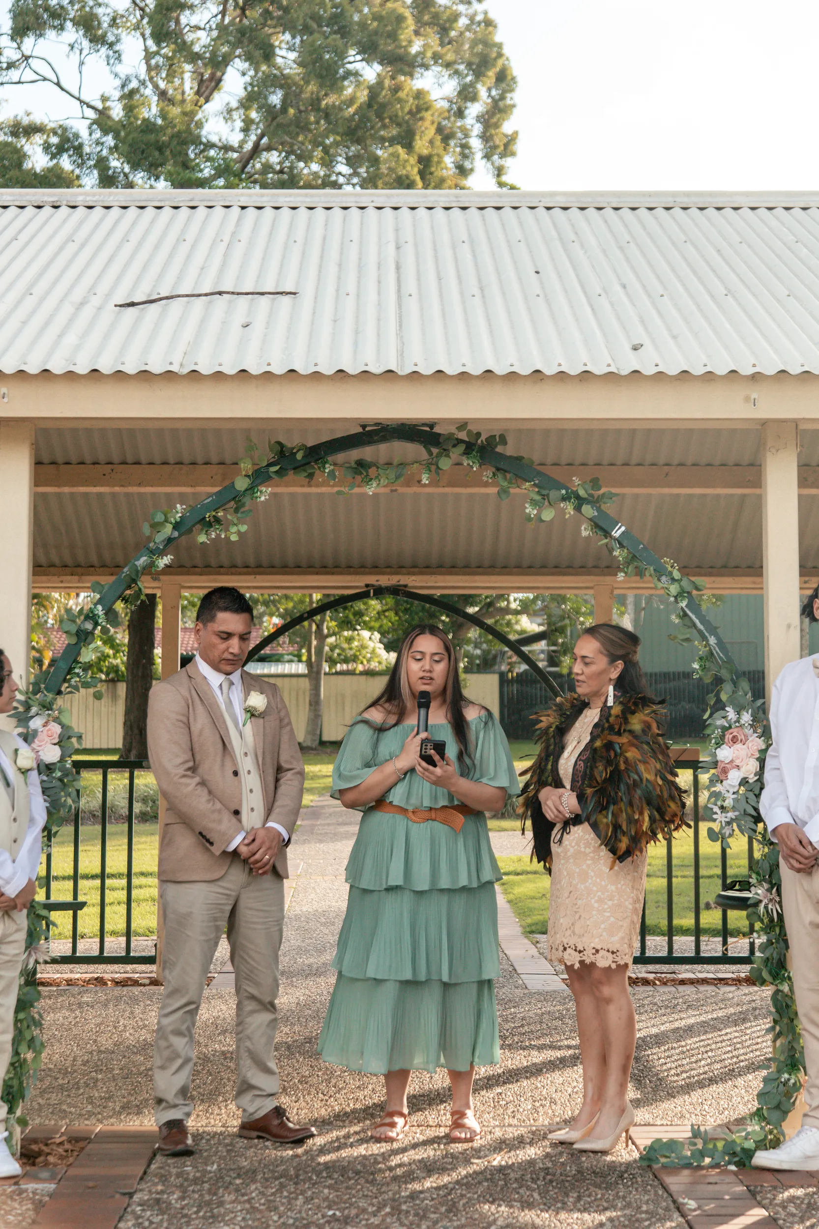 Wedding ceremony under pavilion with officiant speaking and bride in traditional feather cloak