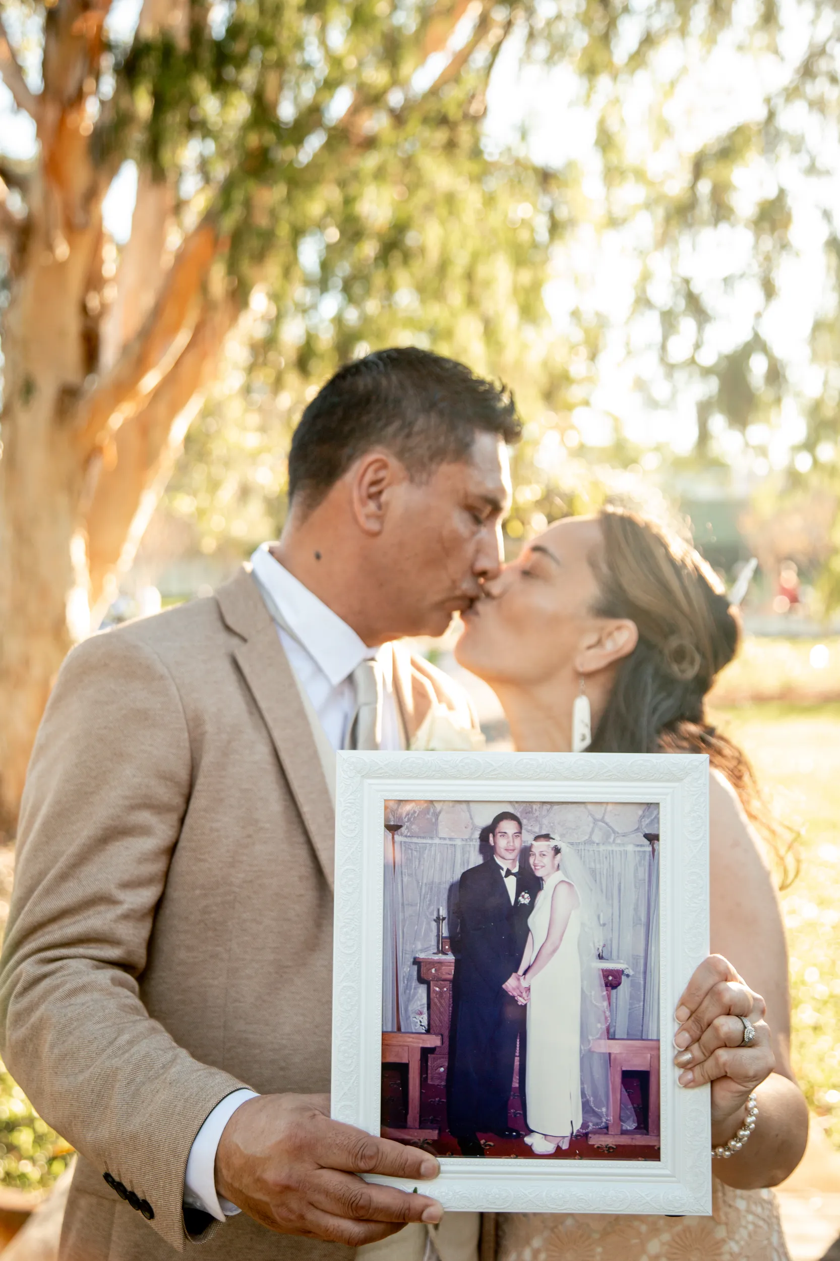 Meaningful vow renewal moment with couple kissing while holding framed photo of their original wedding day