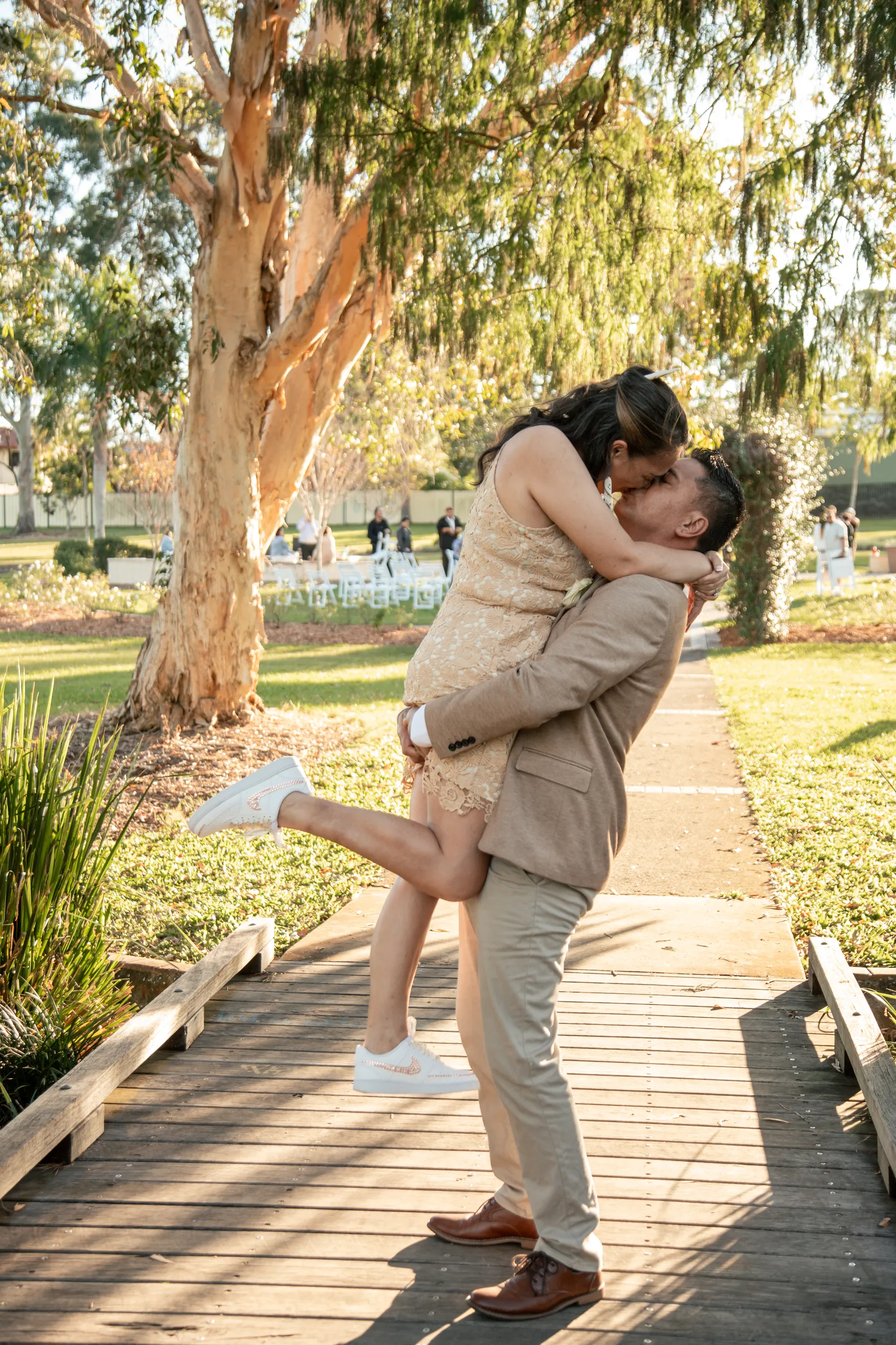 Joyful wedding moment with groom lifting bride in romantic embrace on wooden boardwalk in park setting