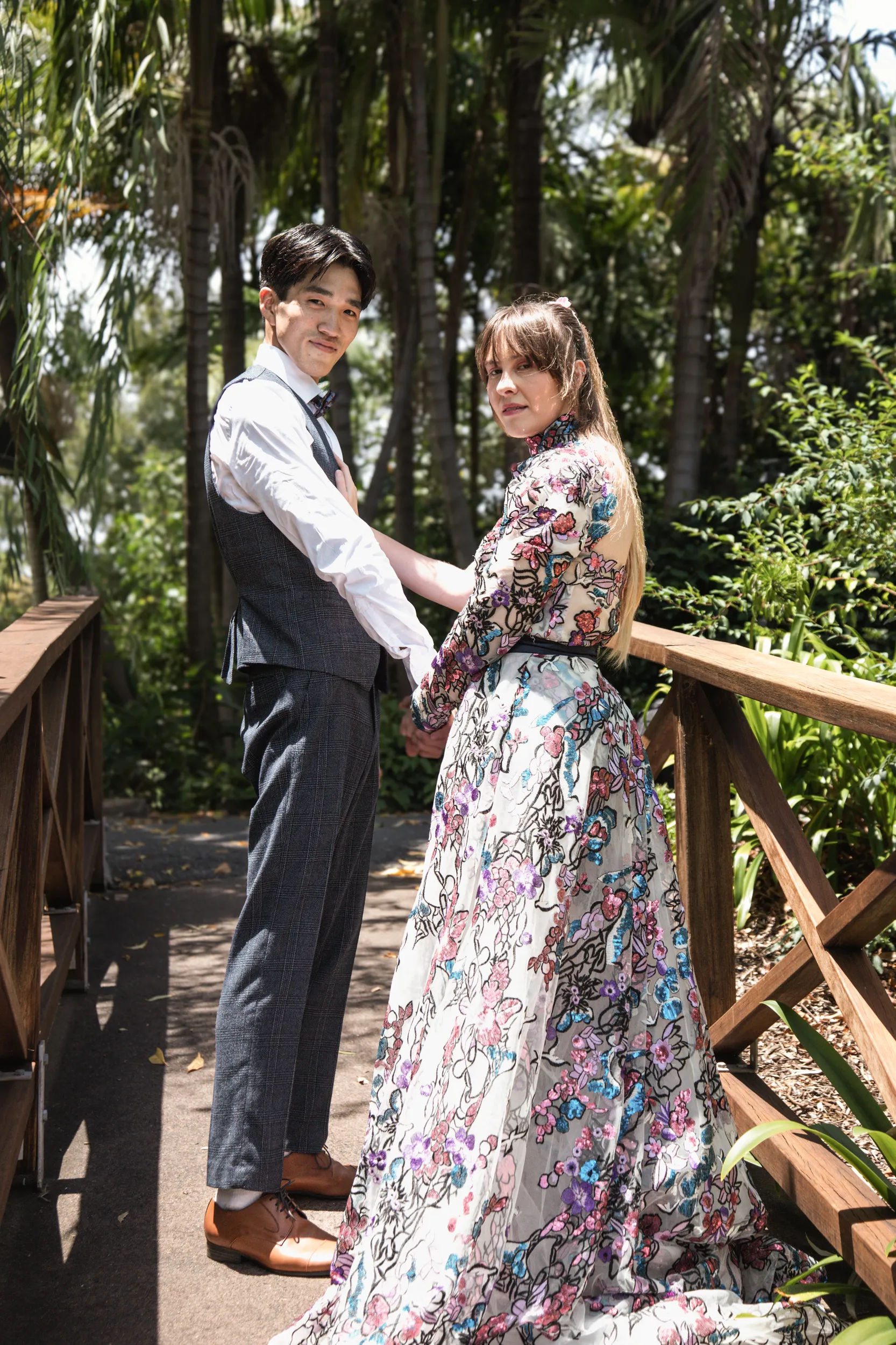 Unique wedding portrait of couple on wooden bridge with bride in colorful floral dress in tropical garden setting